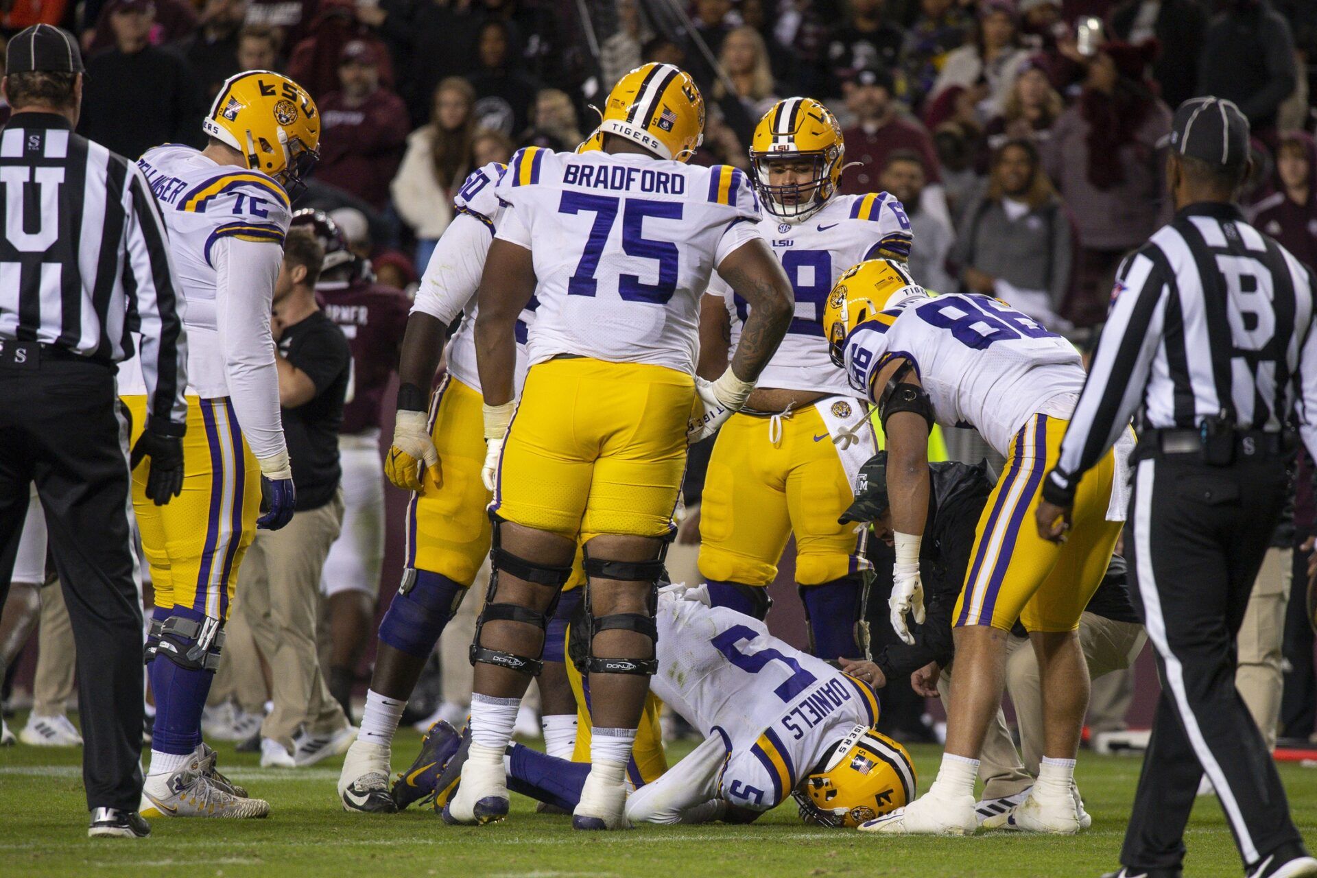 Anthony Bradford, wide receiver Evan Francioni, and offensive lineman Garrett Dellinger check on the injury of quarterback Jayden Daniels.