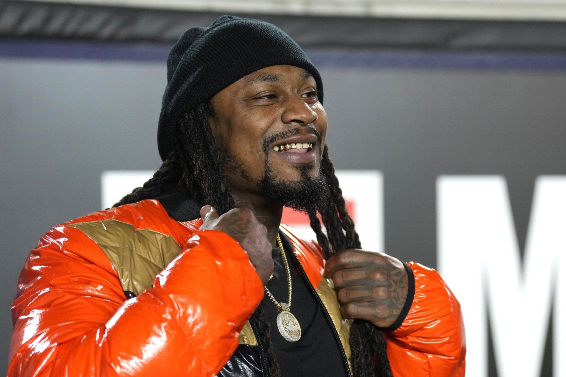 Former NFL running back Marshawn Lynch smiling on the sidelines at a California Bears game.