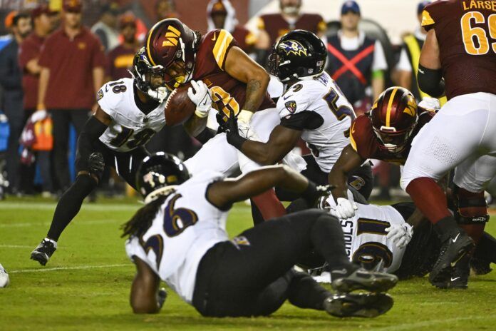 Baltimore Ravens defenders tackle Washington Commanders RB Chris Rodriguez Jr. (23), forcing a fumble.