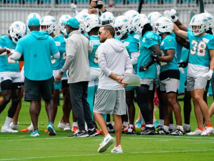 The Miami Dolphins huddle as coaches look on.