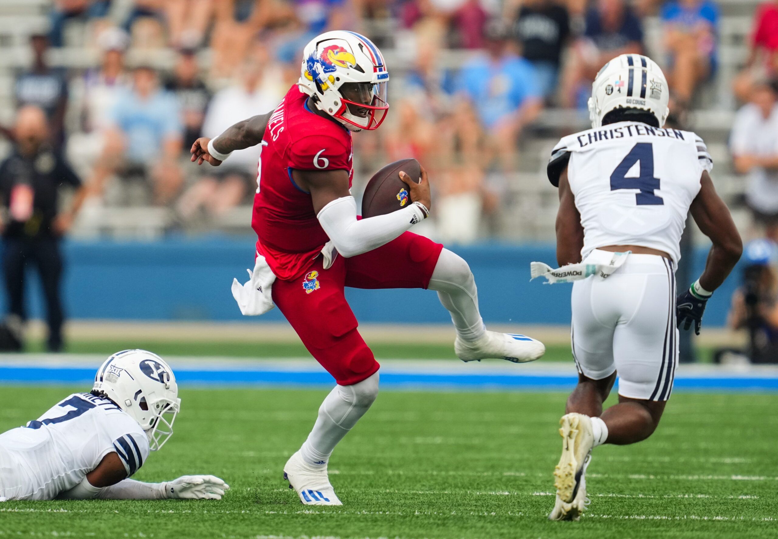 Jalon Daniels (6) runs the ball against Brigham Young Cougars cornerback Kamden Garrett (7) and cornerback Caleb Christensen (4) during the second half at David Booth Kansas Memorial Stadium.
