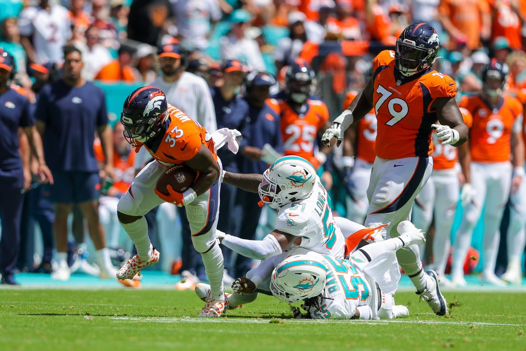 Javonte Williams (33) breaks a tackle from Miami Dolphins linebacker David Long Jr. (51) and linebacker Jerome Baker (55) in the first quarter at Hard Rock Stadium.