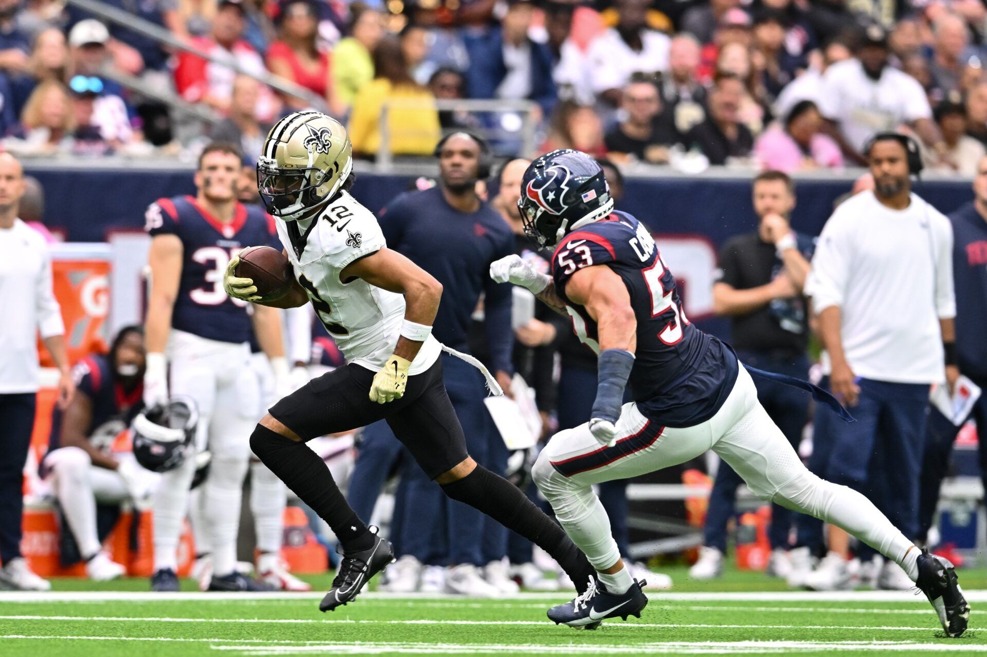 New Orleans Saints wide receiver Chris Olave (12) runs the ball as Houston Texans linebacker Blake Cashman (53) applies pressure.