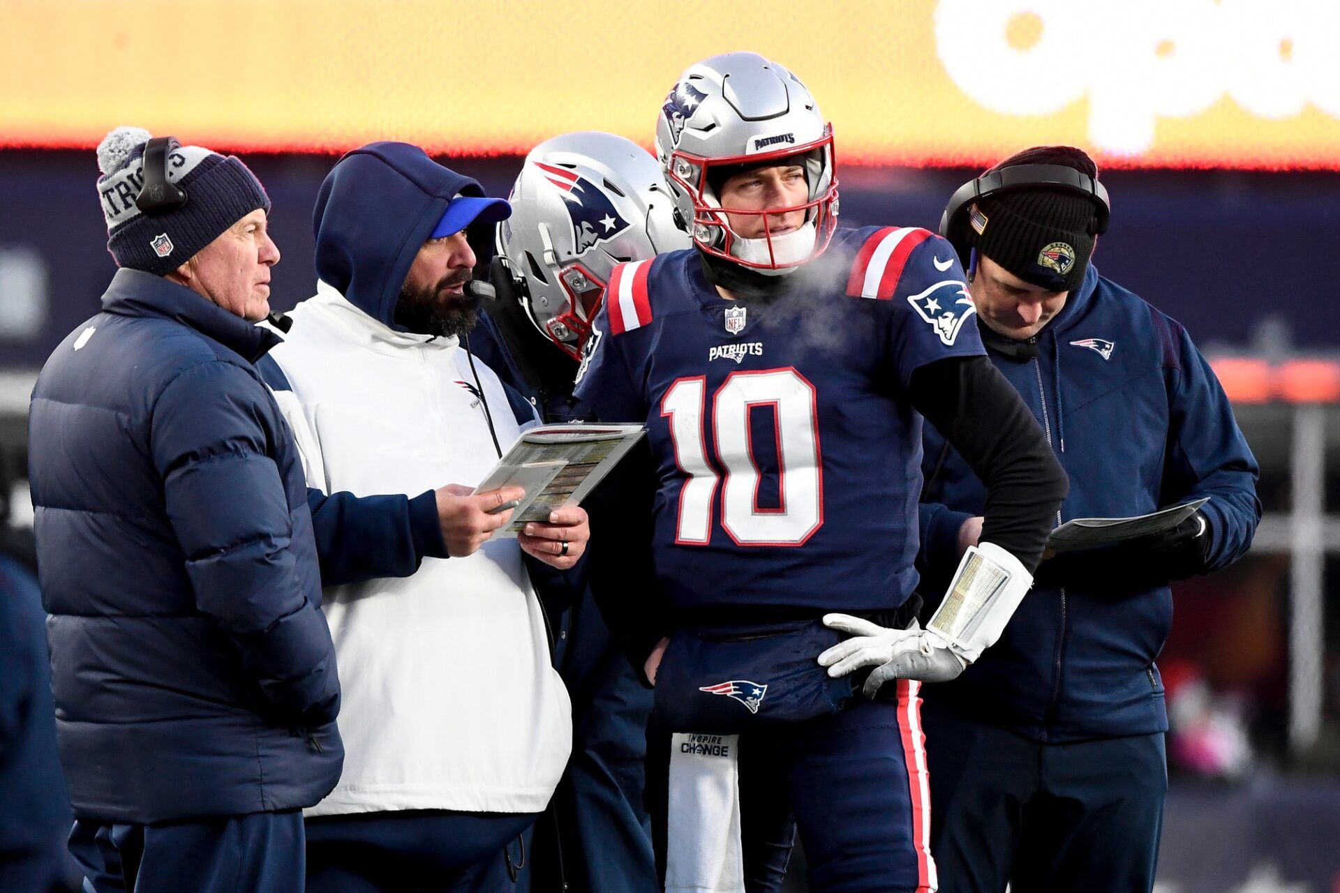 New England Patriots QB Mac Jones (10) talks with head coach Bill Belichick and the coaching staff during a game.