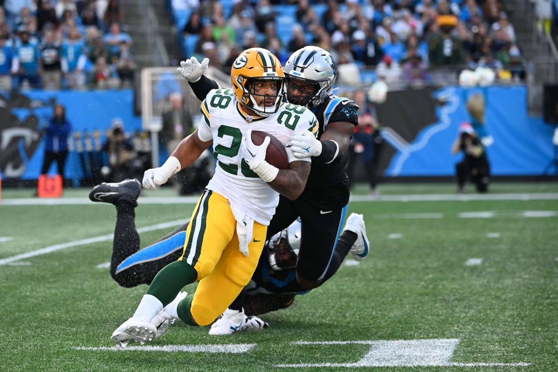 Green Bay Packers running back AJ Dillon (28) with the ball as Carolina Panthers defensive tackle DeShawn Williams (96) and linebacker Brian Burns (0) defend in the fourth quarter at Bank of America Stadium.