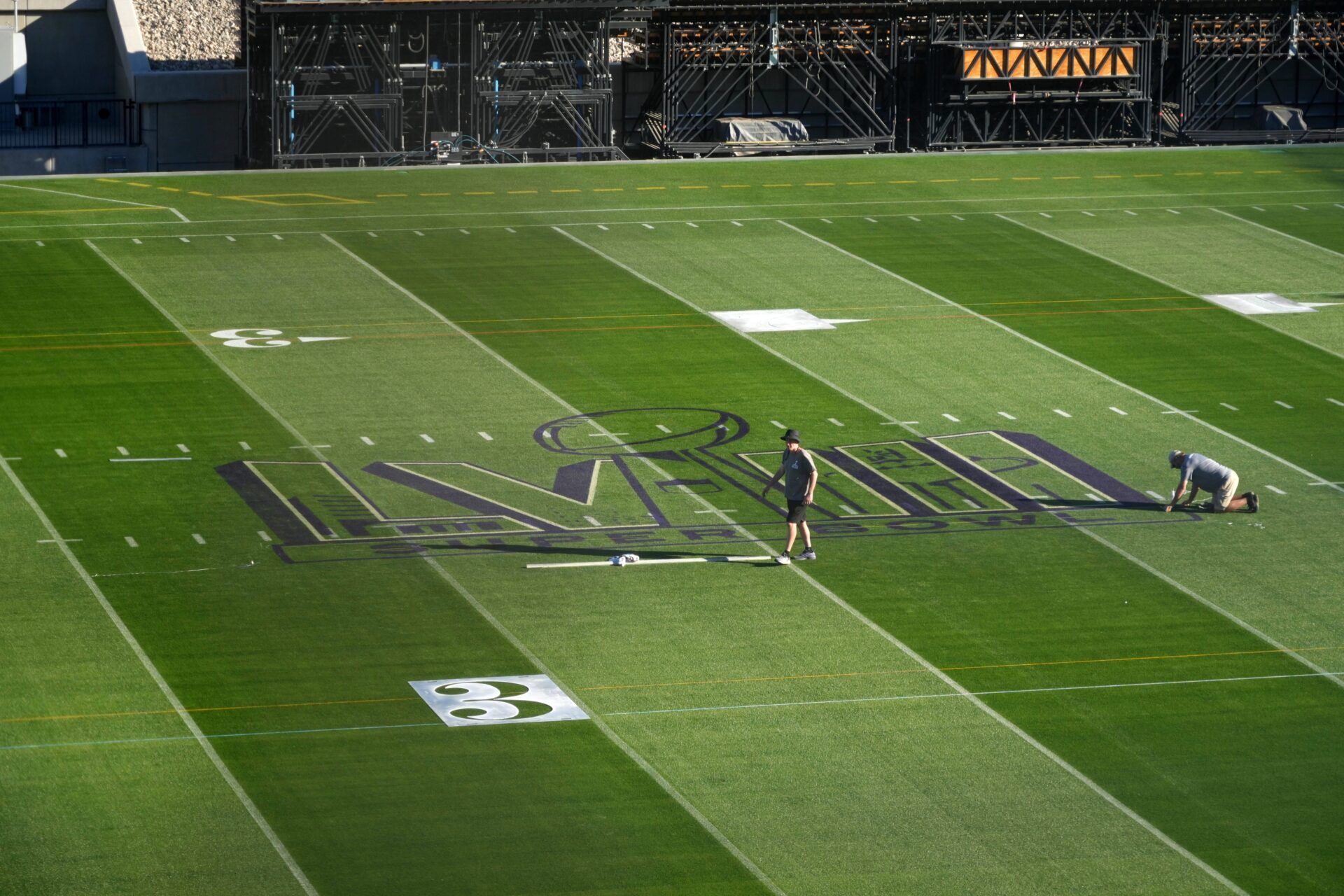 Workers paint the Super Bowl LVIII logo on the field at Allegiant Stadium.