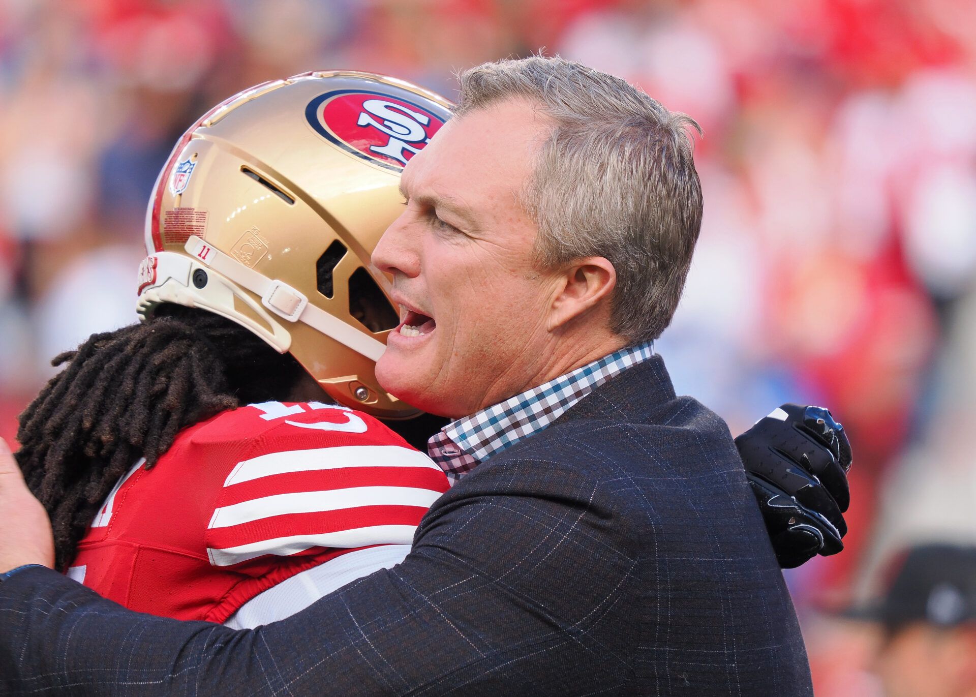 San Francisco 49ers general manager John Lynch hugs a player looks on before the NFC Championship football game against the Detroit Lions at Levi's Stadium.