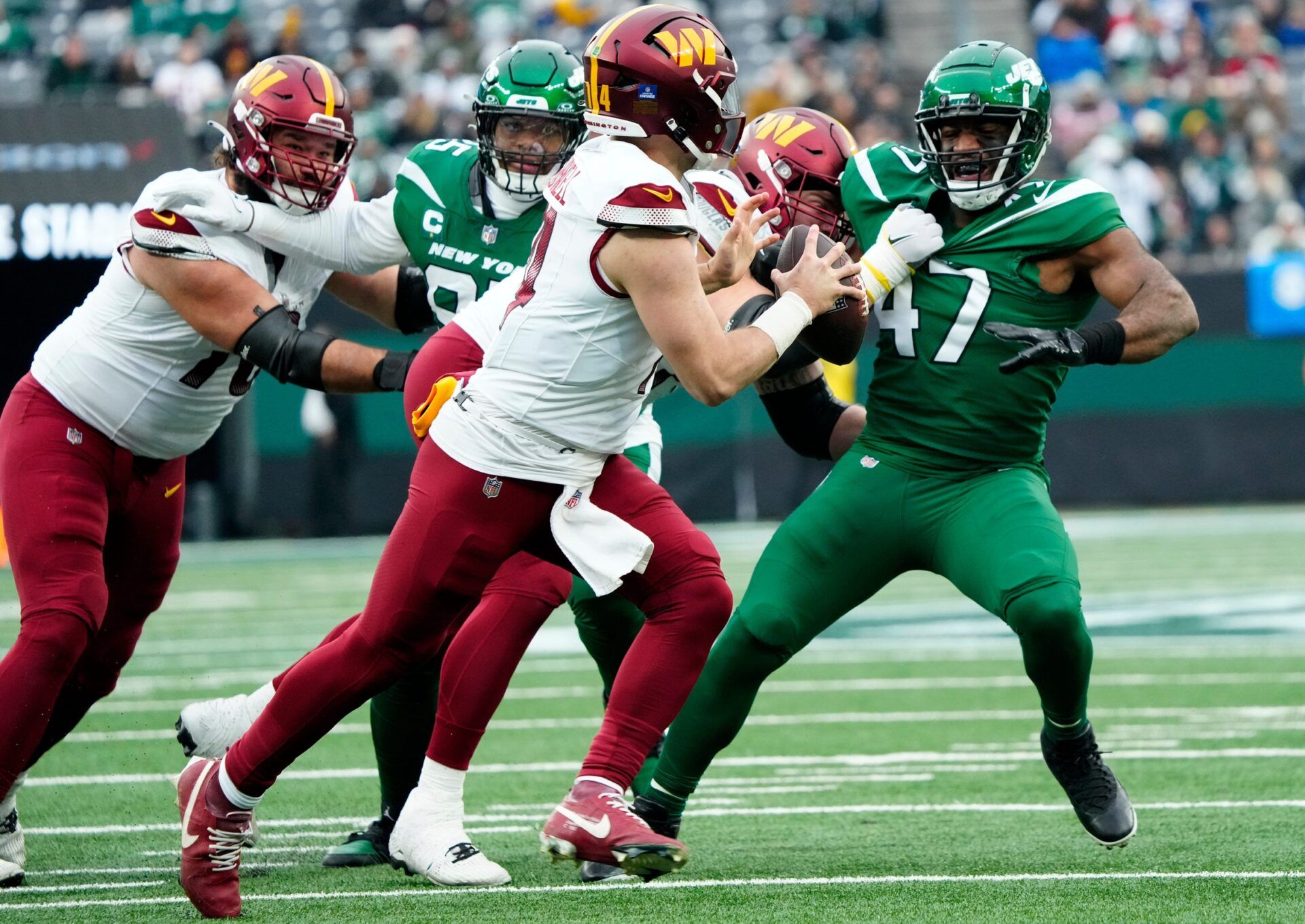 Washington Commanders quarterback Sam Howell (14) looks for an open teammate as New York Jets linebacker Bryce Huff (47) is held back by the offense, at MetLife Stadium.