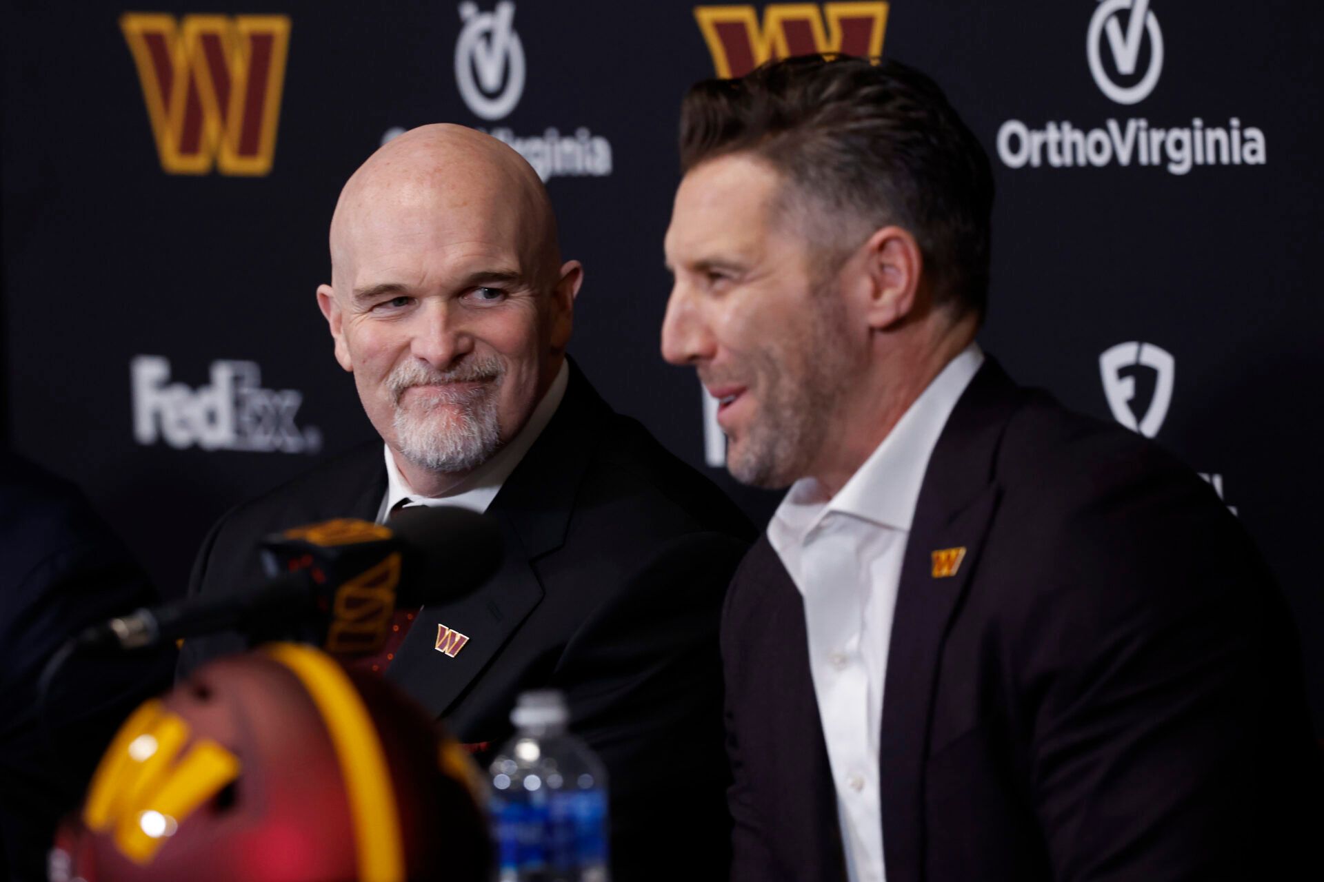 Feb 5, 2024; Ashburn, VA, USA; Washington Commanders head coach Dan Quinn (L) smiles as Commanders general manager Adam Peters (R) speaks during Quinn's introductory press conference at Commanders Park. Mandatory Credit: Geoff Burke-USA TODAY Sports