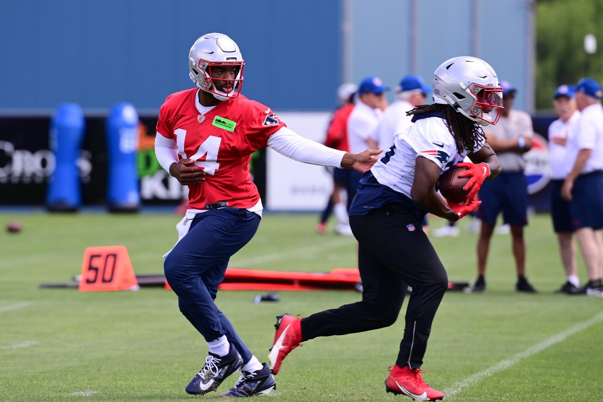 New England Patriots QB Jacoby Brissett (14) hands the ball off to RB Rhamondre Stevenson (38) during practice.