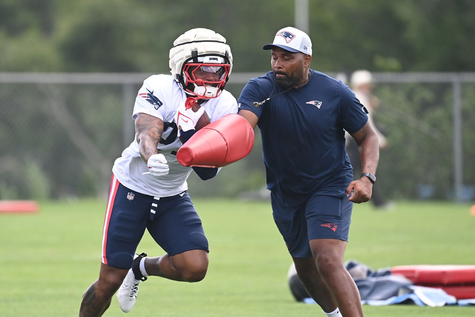 New England Patriots head coach Jerod Mayo works with RB Antonio Gibson (21) in a drill during training camp.