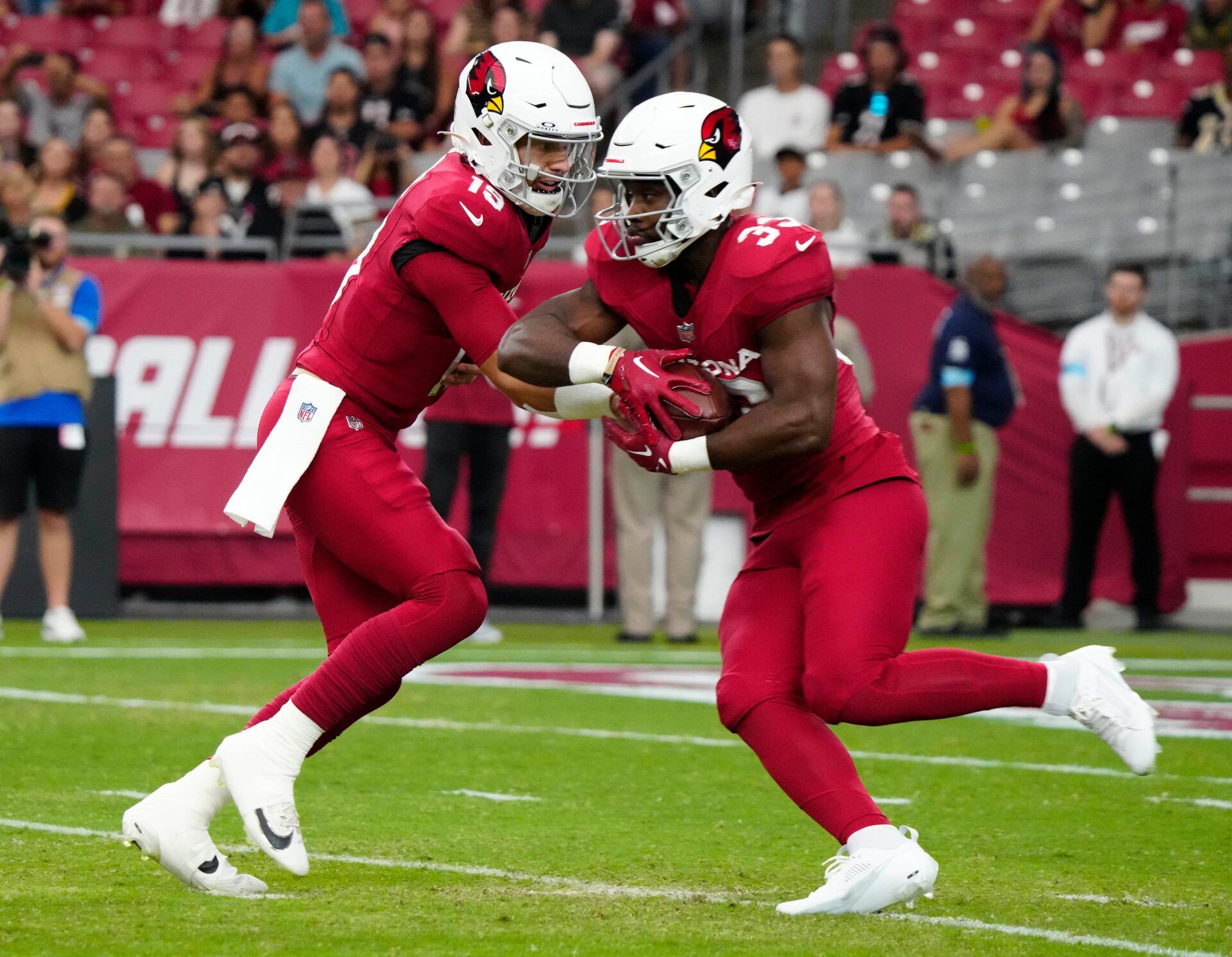 Cardinals quarterback Desmond Ridder (19) hands the ball off to running back Trey Benson (33) against the Saints during a game at State Farm Stadium in Glendale, Ariz., on Saturday, Aug. 10, 2024.