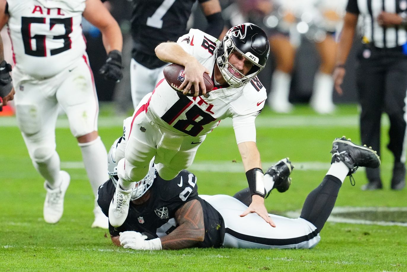 Atlanta Falcons quarterback Kirk Cousins (18) is tripped up by Las Vegas Raiders defensive tackle Jonah Laulu (96) during the second quarter at Allegiant Stadium.