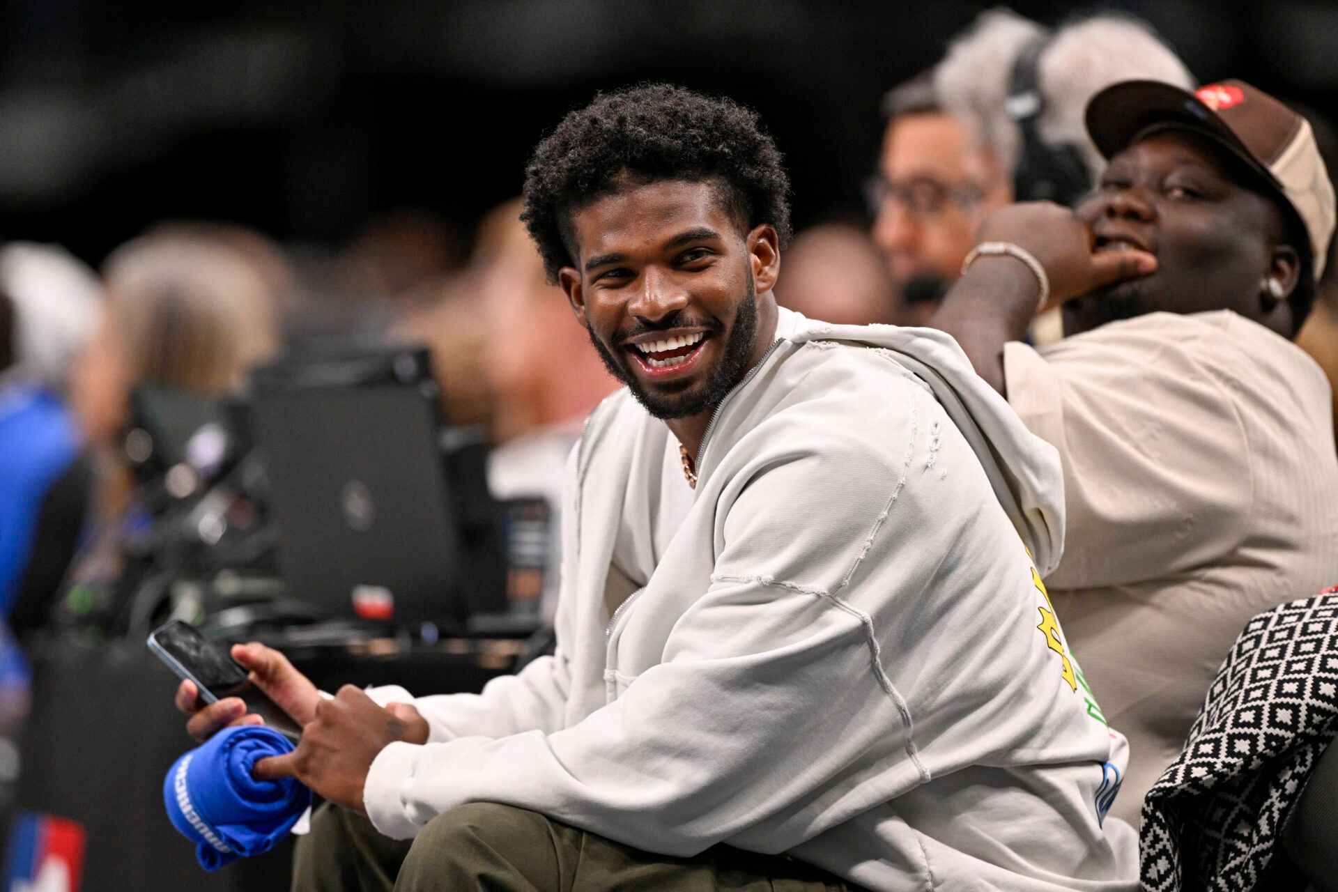 Jan 14, 2025; Dallas, Texas, USA; Colorado Buffaloes quarterback Shedeur Sanders laughs as he watches the game between the Dallas Mavericks and the Denver Nuggets during the second half at the American Airlines Center. Mandatory Credit: Jerome Miron-Imagn Images