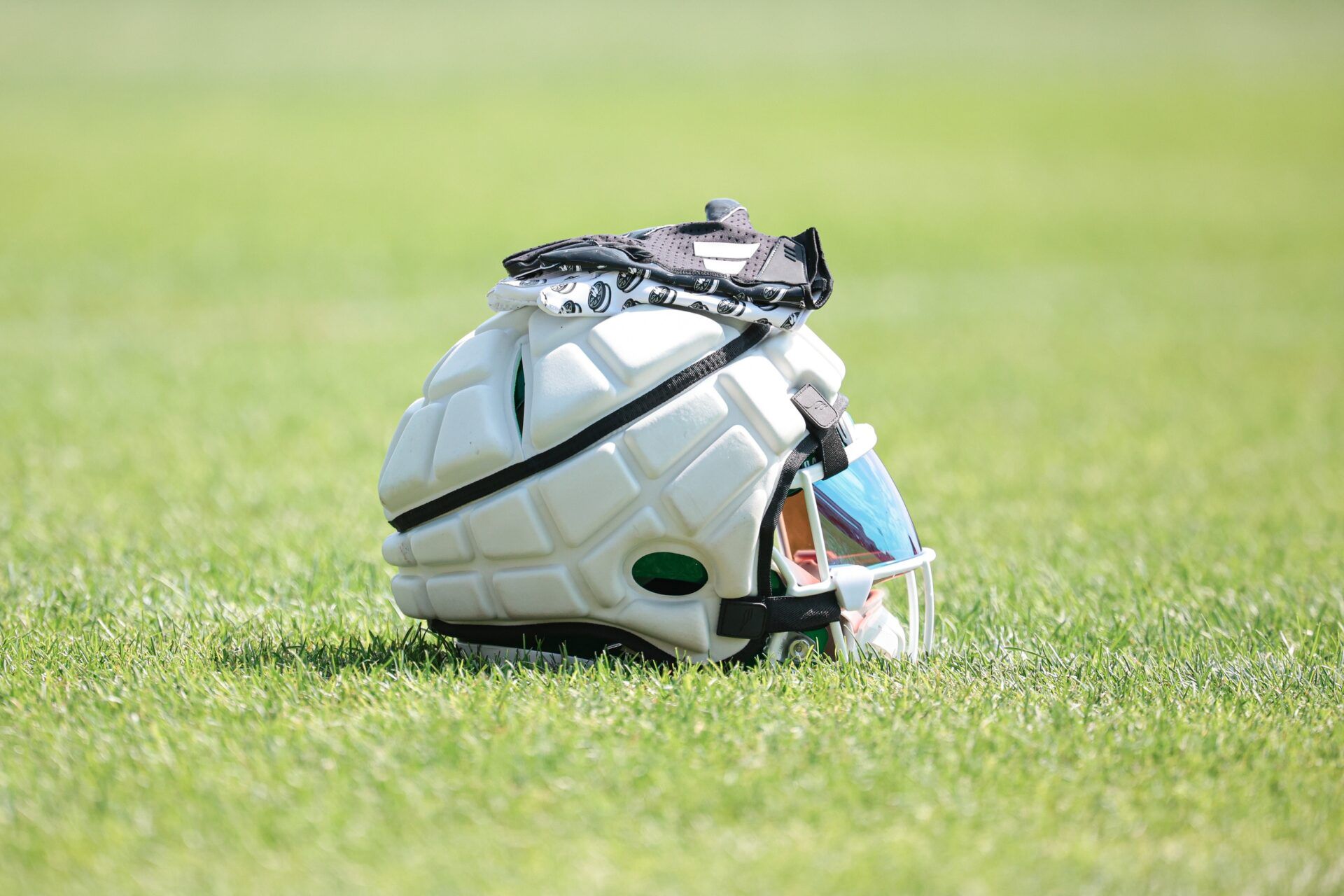 A helmet covered by a guardian cap and gloves rests on the field during training camp.