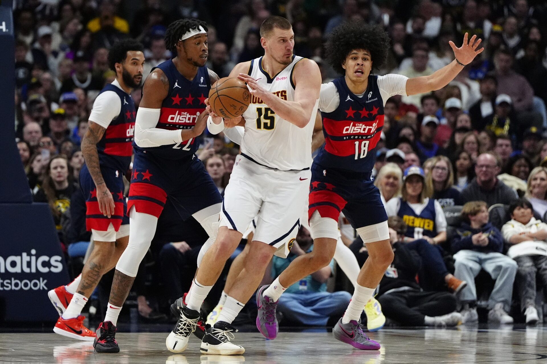 Washington Wizards forward Richaun Holmes (22) and forward Kyshawn George (18) defend on Denver Nuggets center Nikola Jokic (15) in the second half at Ball Arena.