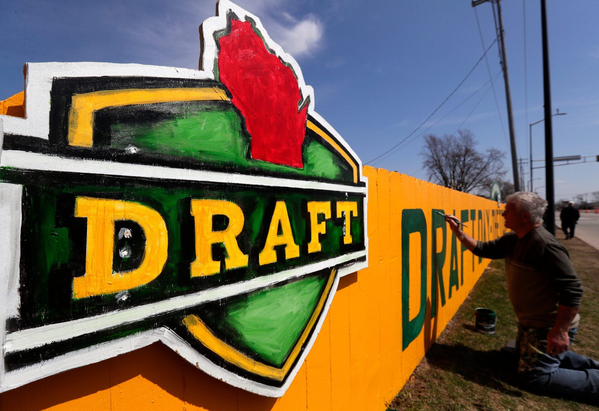 Christopher Handler paints a new 2025 NFL Draft-themed fence along Lombardi Avenue on April 12, 2025, in Green Bay, Wis.