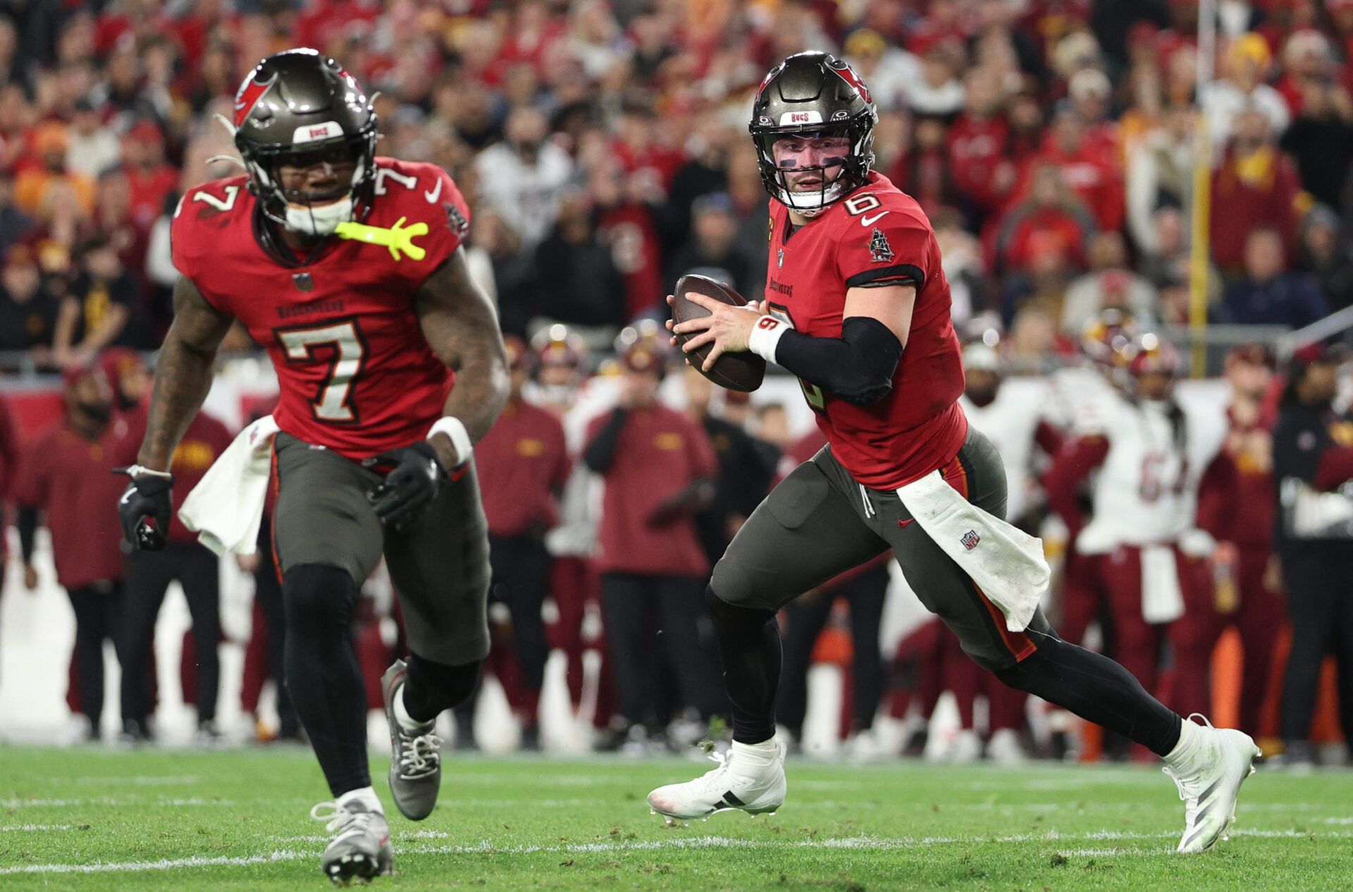 Tampa Bay Buccaneers quarterback Baker Mayfield (6) rolls out behind running back Bucky Irving (7)  during the third quarter of a NFC wild card playoff against the Washington Commanders at Raymond James Stadium.