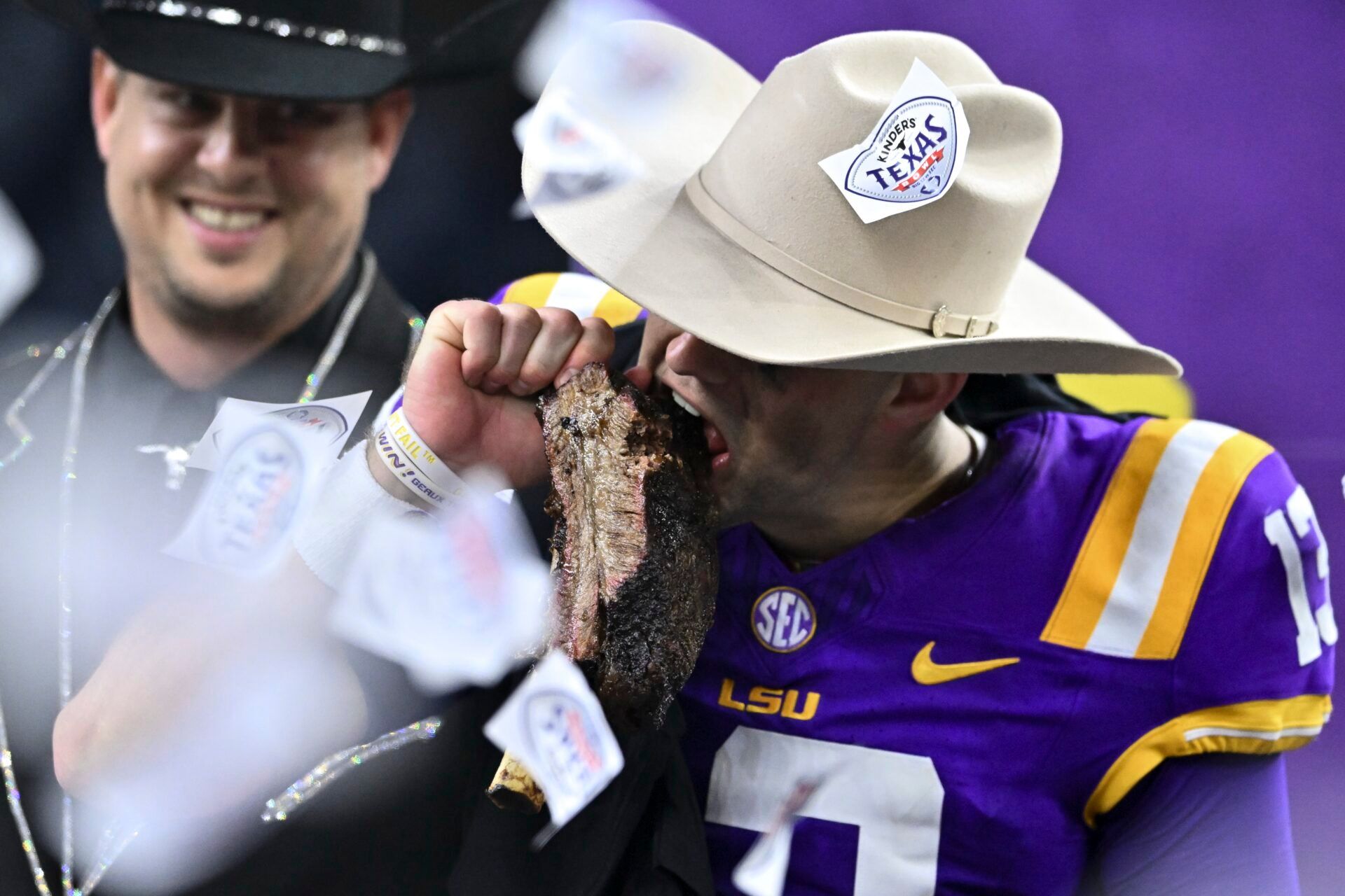 LSU Tigers quarterback Garrett Nussmeier (13) takes a bite of the Kinder’s BBQ rib during the post game celebration at NRG Stadium. The Tigers defeat the Bears 44-31.