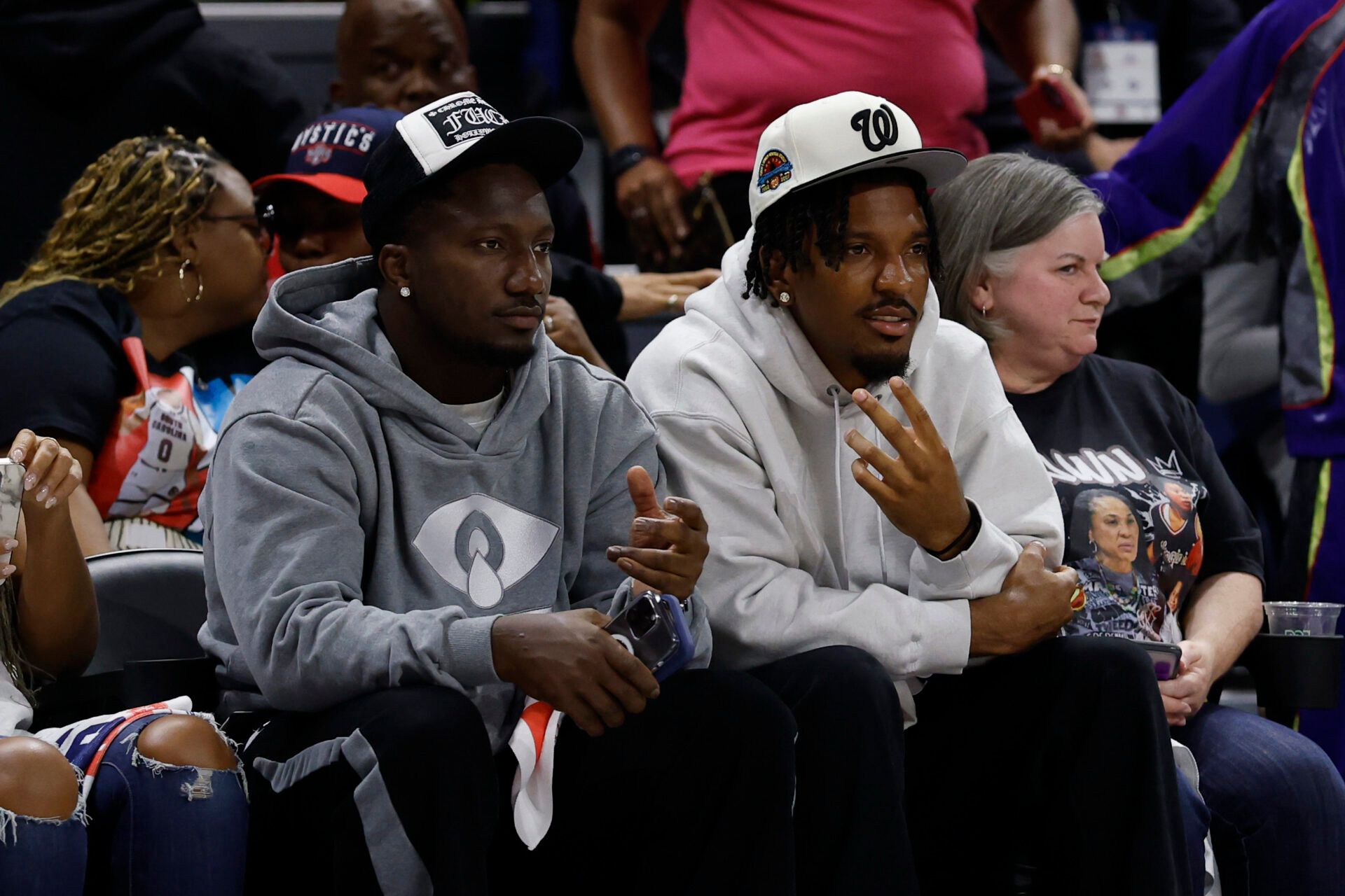Washington Commanders wide receiver Deebo Samuels (L) and Commanders quarterback Jayden Daniels (R) wave to the crowd from courts wide during the game between the Washington Mystics and Atlanta Dream at CareFirst Arena.
