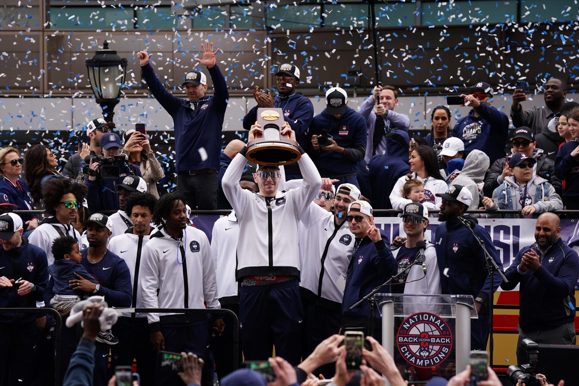 UConn Huskies center Donovan Clingan (32) hold up the championship trophy as the team celebrates in front of a large crowd of fans after the teams victory parade.