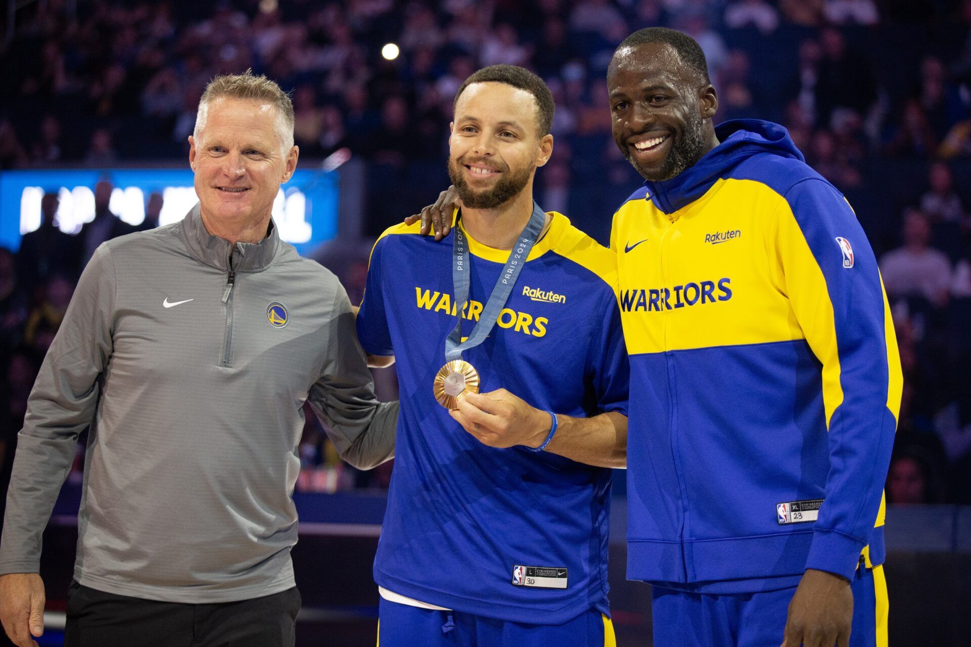 Golden State Warriors guard Stephen Curry (center) is flanked by head coach Steve Kerr and forward Draymond Green as he is presented his gold medal for his performance for Team USA at the 2024 Summer Olympics in Paris before taking on the Sacramento Kings at Chase Center.