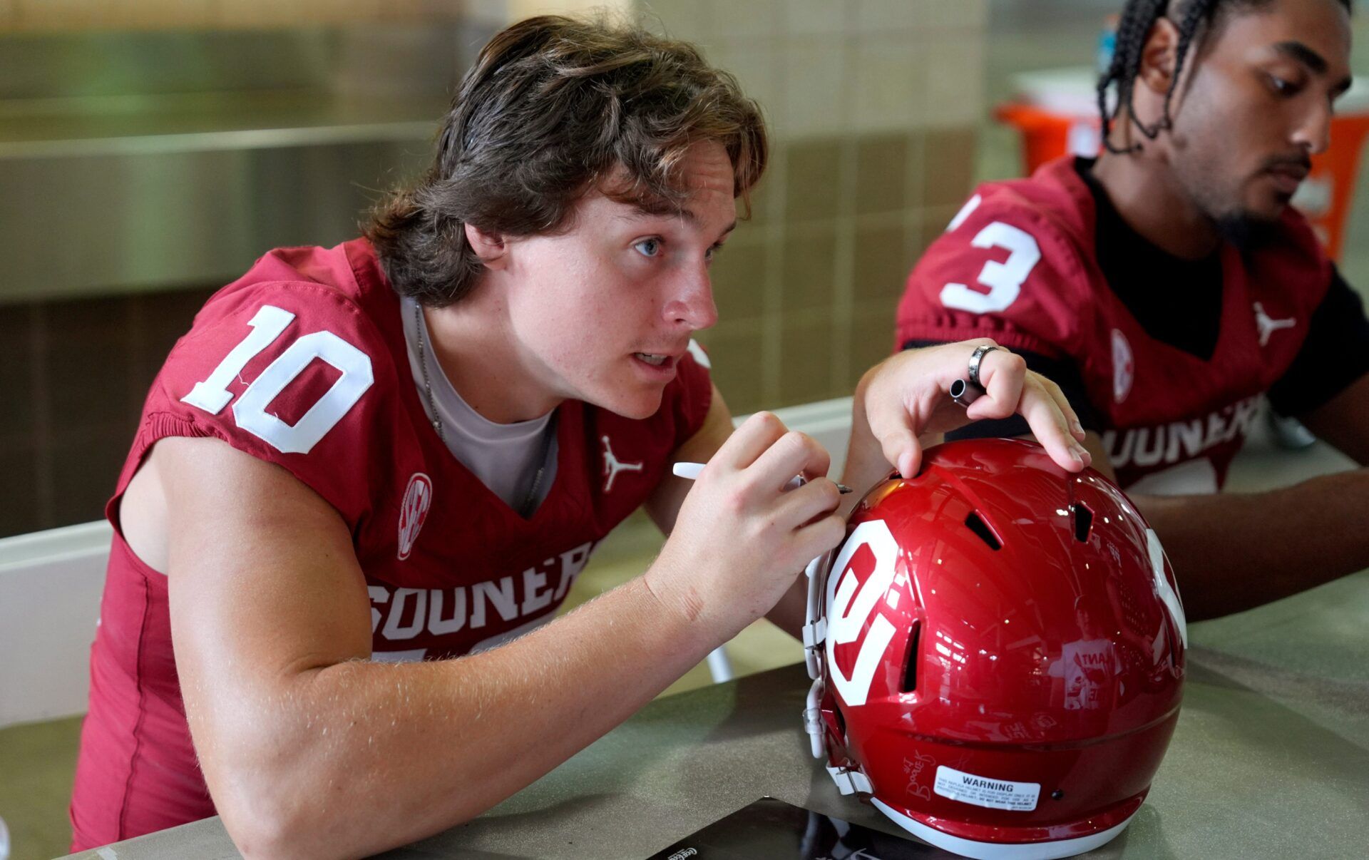 Oklahoma Sooners quarterback John Mateer (10) signs a helmet for a fan during Meet the Sooners Day at Gaylord Family Ñ Oklahoma Memorial Stadium, Saturday, Aug. 2, 2025.