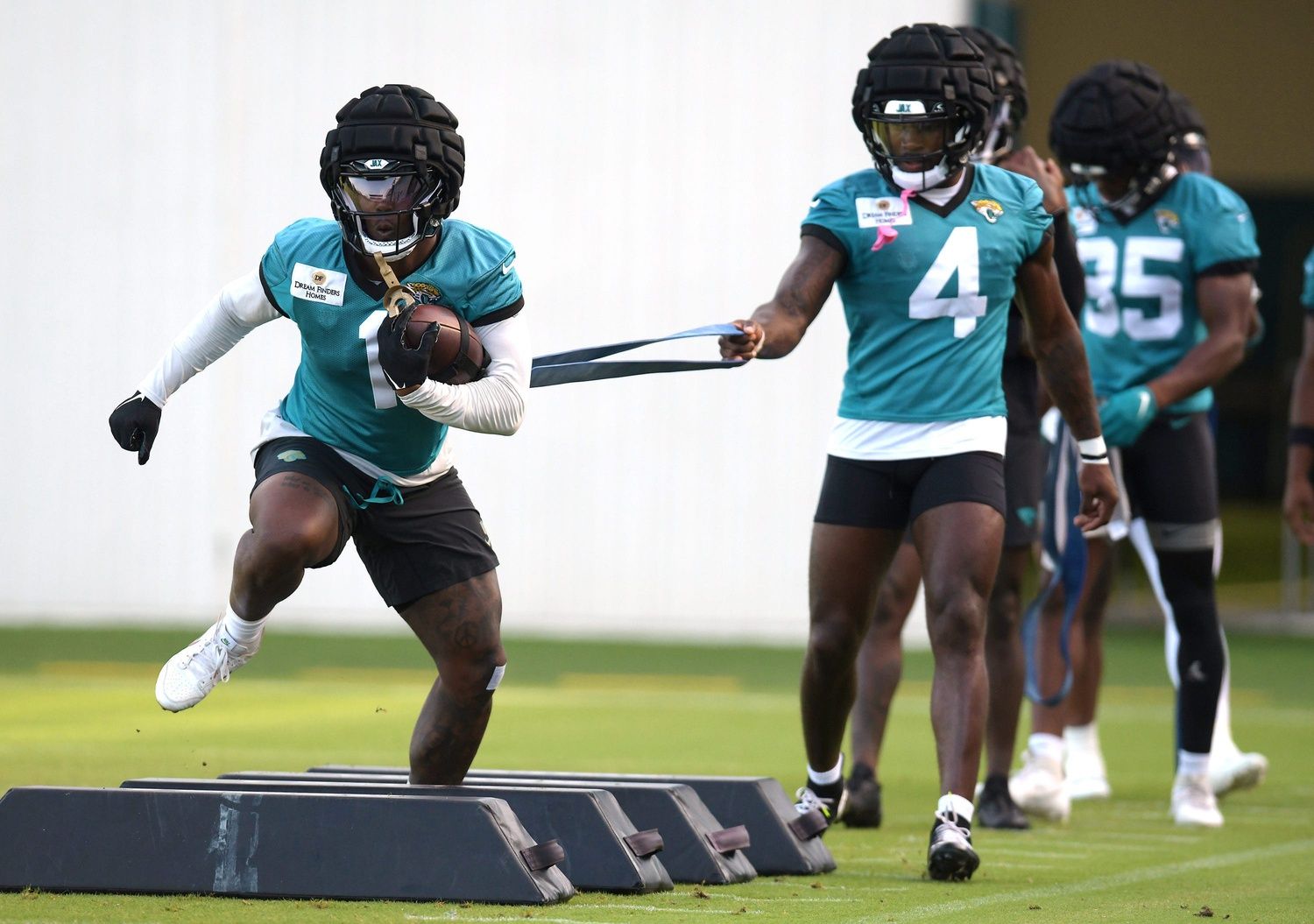 Jacksonville Jaguars running back Tank Bigsby (4) holds the elastic band attached to running back Travis Etienne Jr. (1) as they go through drills on the fifth day of the NFL football training camp practice session Monday, July 29, 2024 at EverBank Stadium's Miller Electric Center in Jacksonville, Fla..
