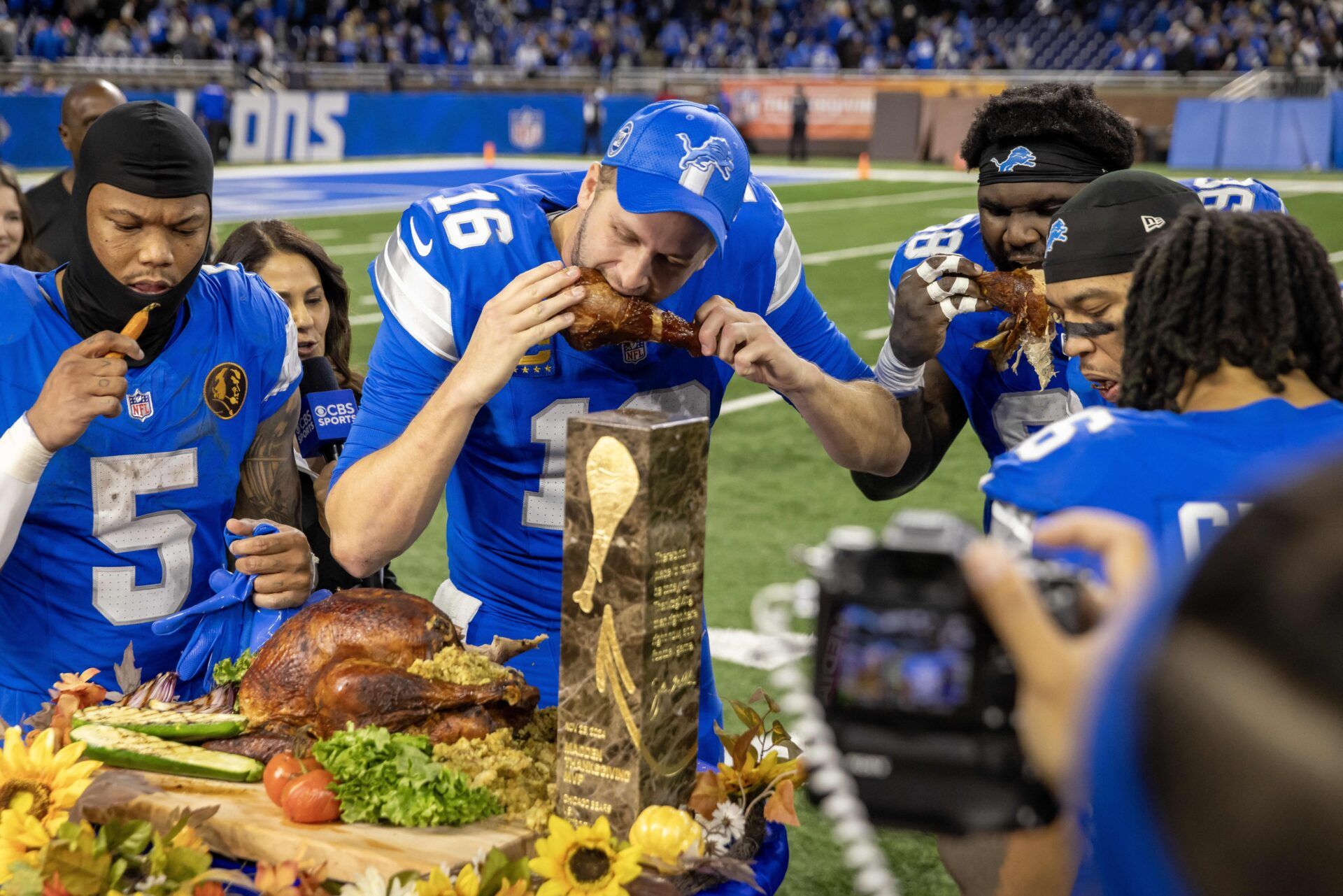 Detroit Lions quarterback Jared Goff (16) takes a bite of the John Madden MVP Turkey with teammates after the annual Thanksgiving Day game defeating the Chicago Bears at Ford Field.