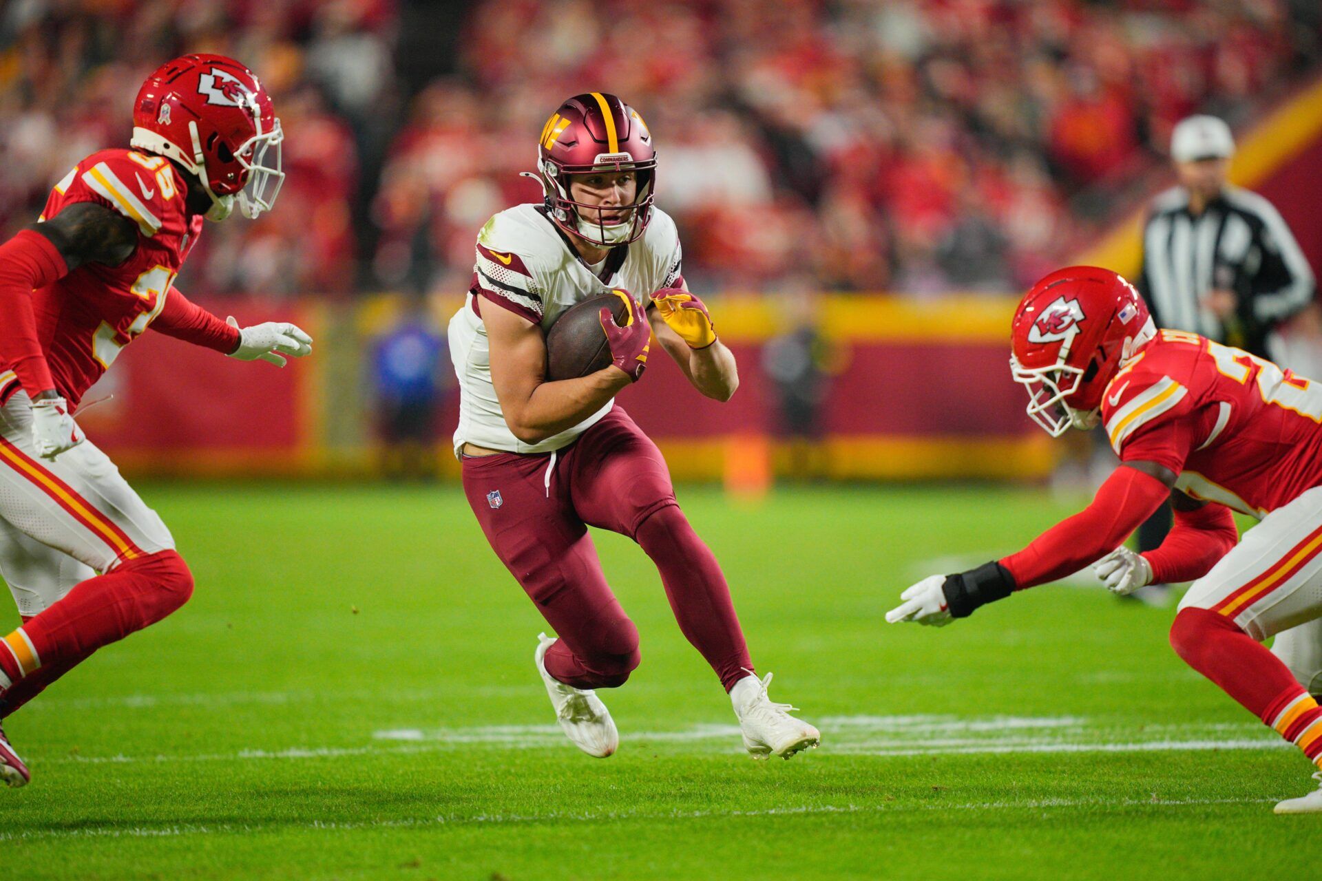 Washington Commanders wide receiver Luke McCaffrey (11) carries the ball defended by Kansas City Chiefs cornerback Jaylen Watson (35) and defensive back Chamarri Conner (27) during the first quarter of the game at GEHA Field at Arrowhead Stadium.