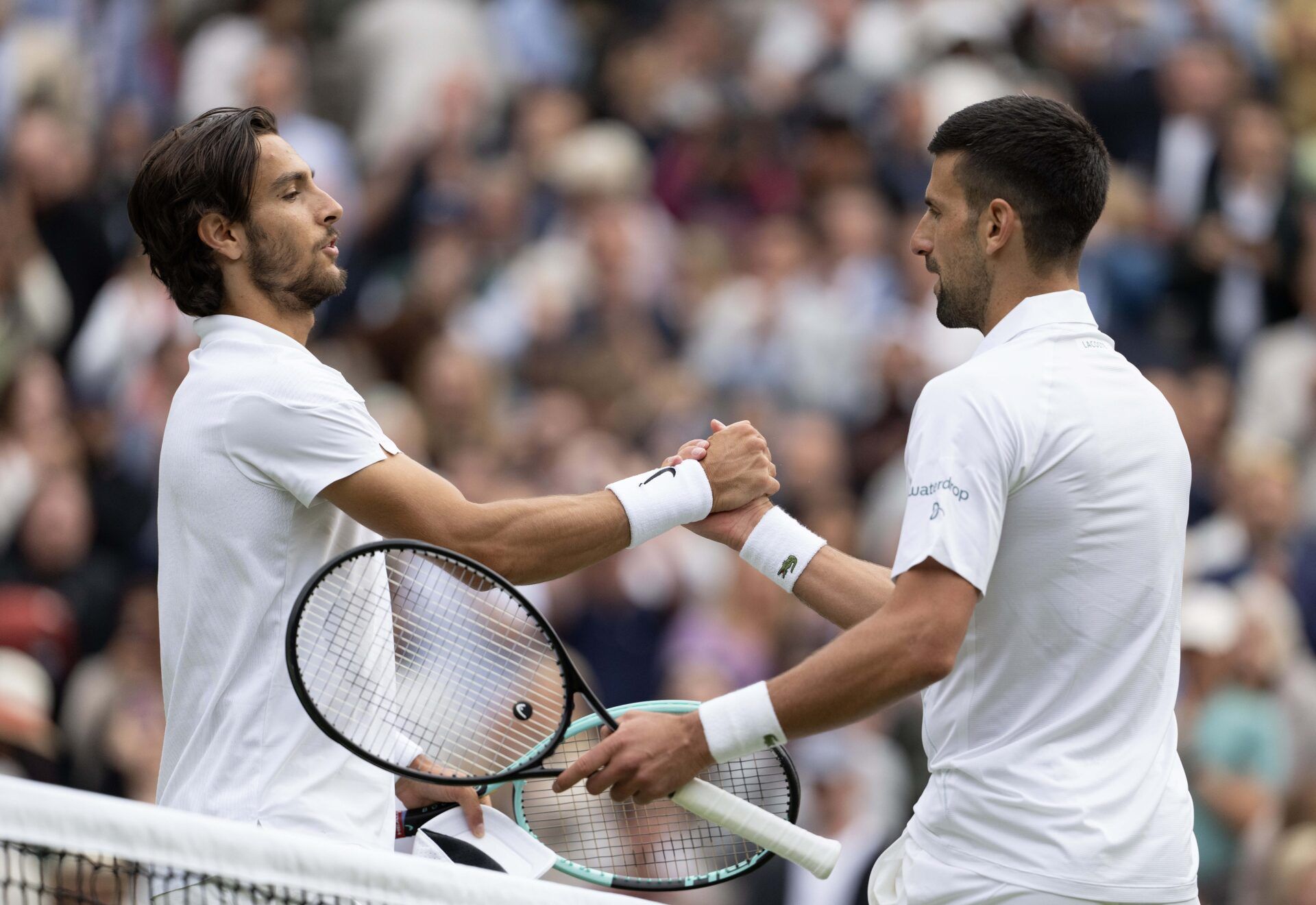 Novak Djokovic of Serbia shakes hands with Lorenzo Musetti of Italy at the net after their match on day 12 at All England Lawn Tennis and Croquet Club.