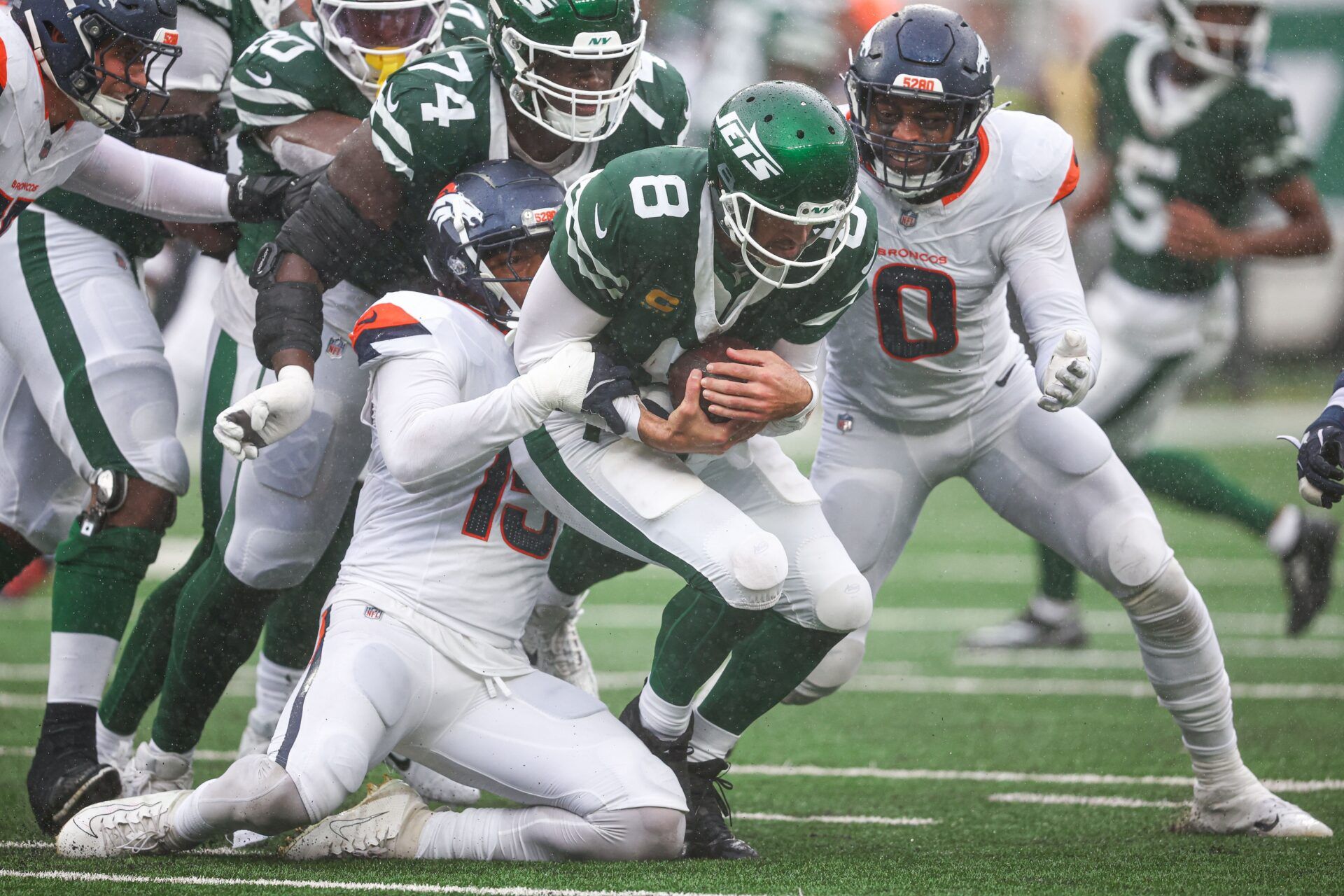 New York Jets quarterback Aaron Rodgers (8) is tackled by Denver Broncos linebacker Nik Bonitto (15) and linebacker Jonathon Cooper (0) during the first half at MetLife Stadium.