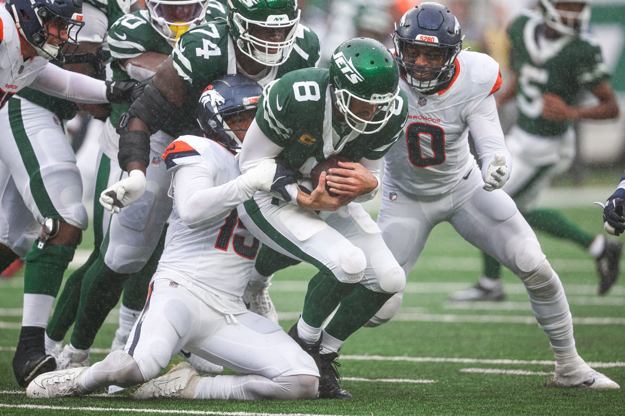 New York Jets quarterback Aaron Rodgers (8) is tackled by Denver Broncos linebacker Nik Bonitto (15) and linebacker Jonathon Cooper (0) during the first half at MetLife Stadium.