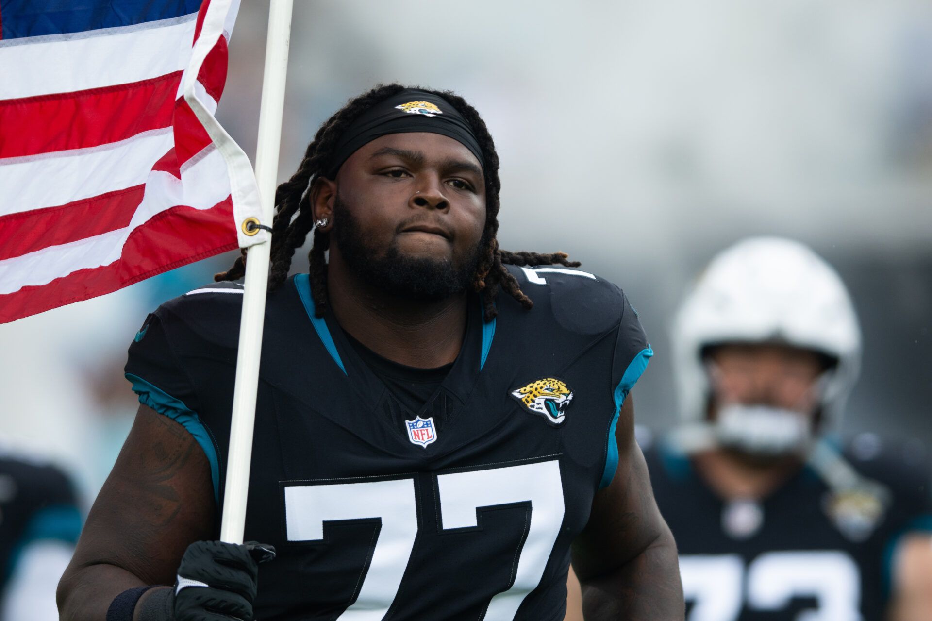 Jacksonville Jaguars offensive lineman Anton Harrison (77) runs onto the field with the American flag before the. game against the Minnesota Vikings at EverBank Stadium.