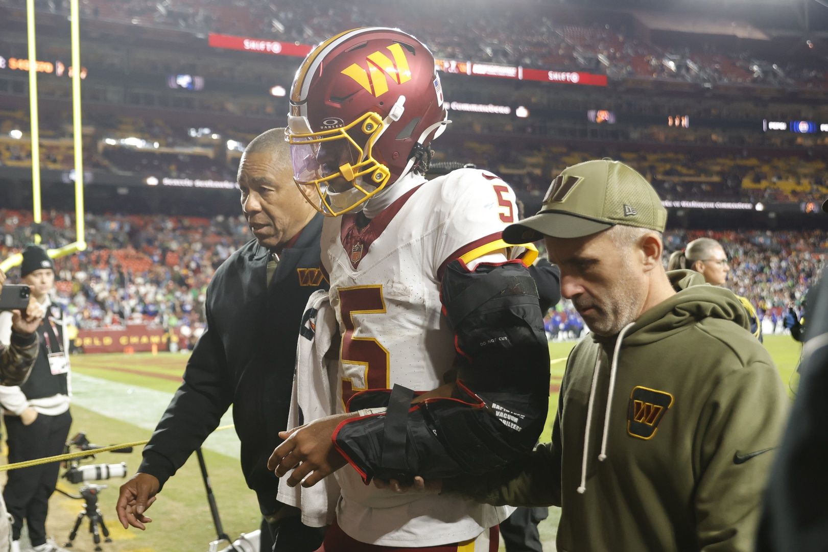 Washington Commanders quarterback Jayden Daniels (5) is helped off the field after an injury during the second half against the Seattle Seahawks at Northwest Stadium.