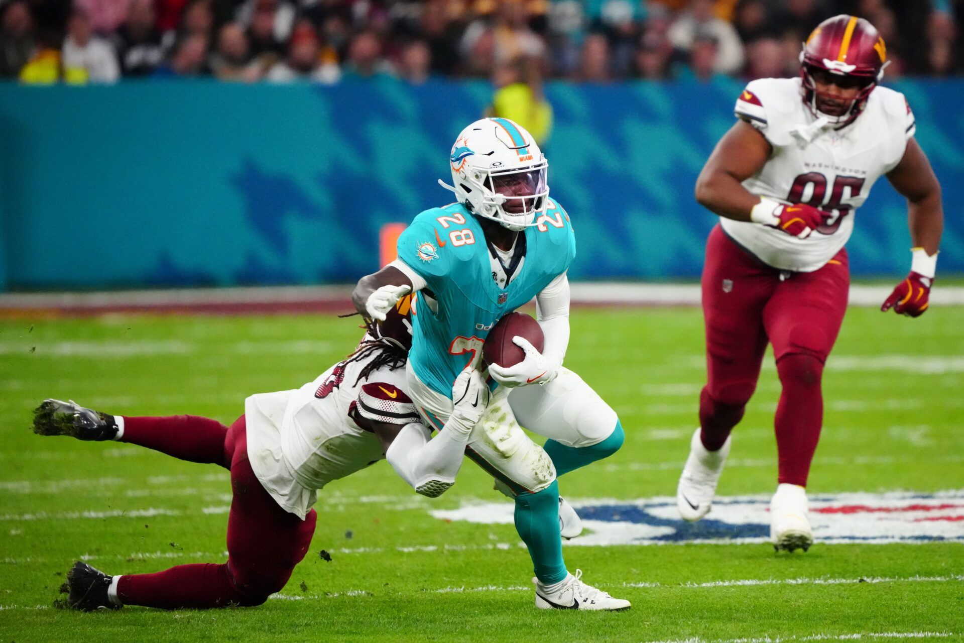 Miami Dolphins running back De'Von Achane (28) carries the ball defended by Washington Commanders linebacker Jordan Magee (58) in the second quarter during the 2025 NFL Madrid Game at Santiago Bernabeu Stadium.