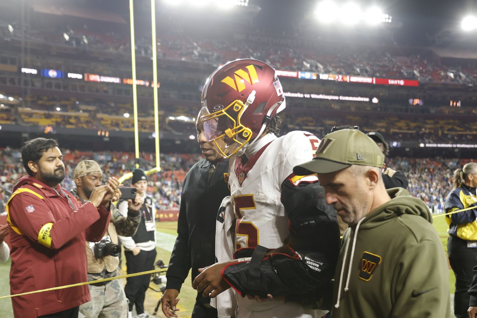 Washington Commanders quarterback Jayden Daniels (5) is helped off the field after an injury during the second half against the Seattle Seahawks at Northwest Stadium.