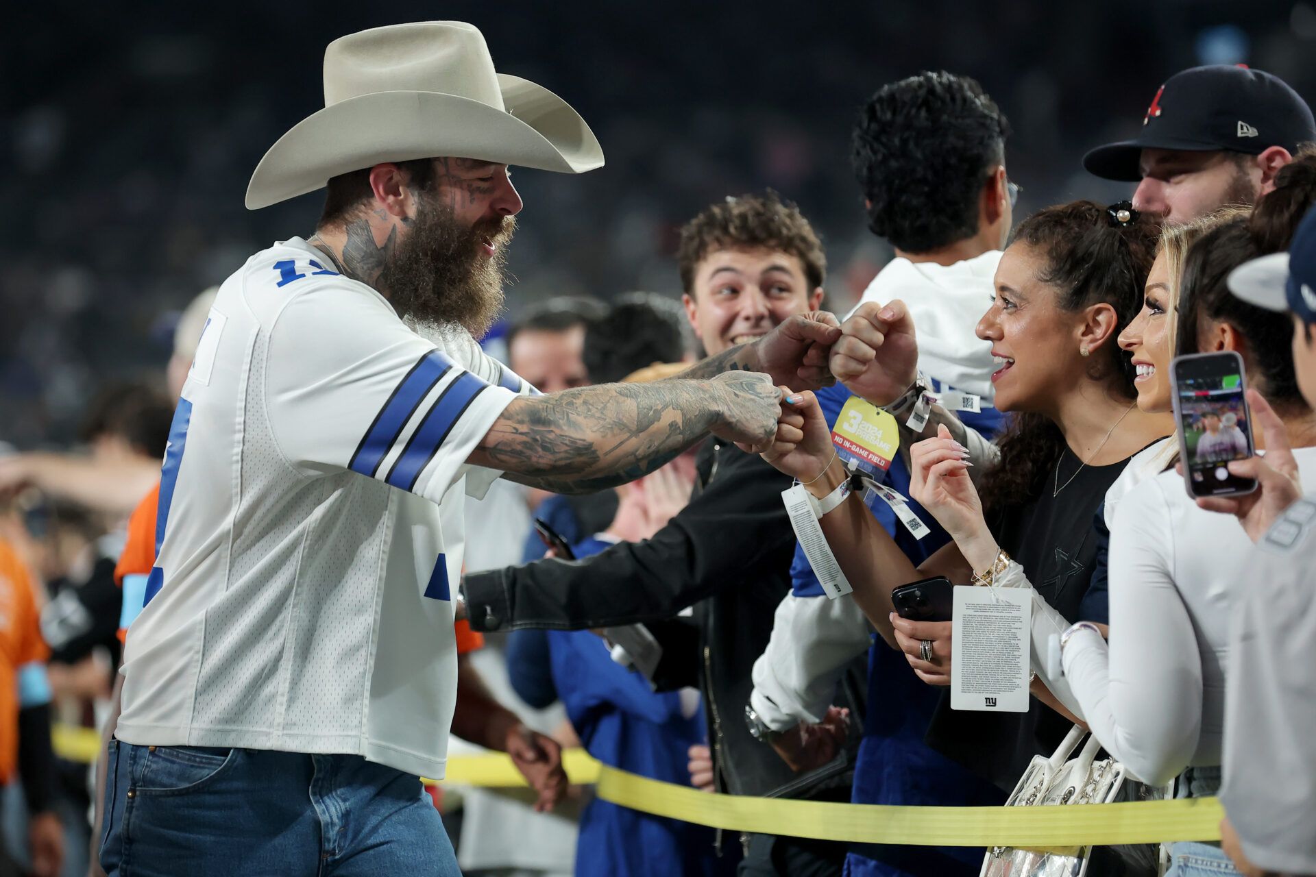 American recording artist Post Malone (left) fist bumps fans on the field before a game between the New York Giants and the Dallas Cowboys at MetLife Stadium.