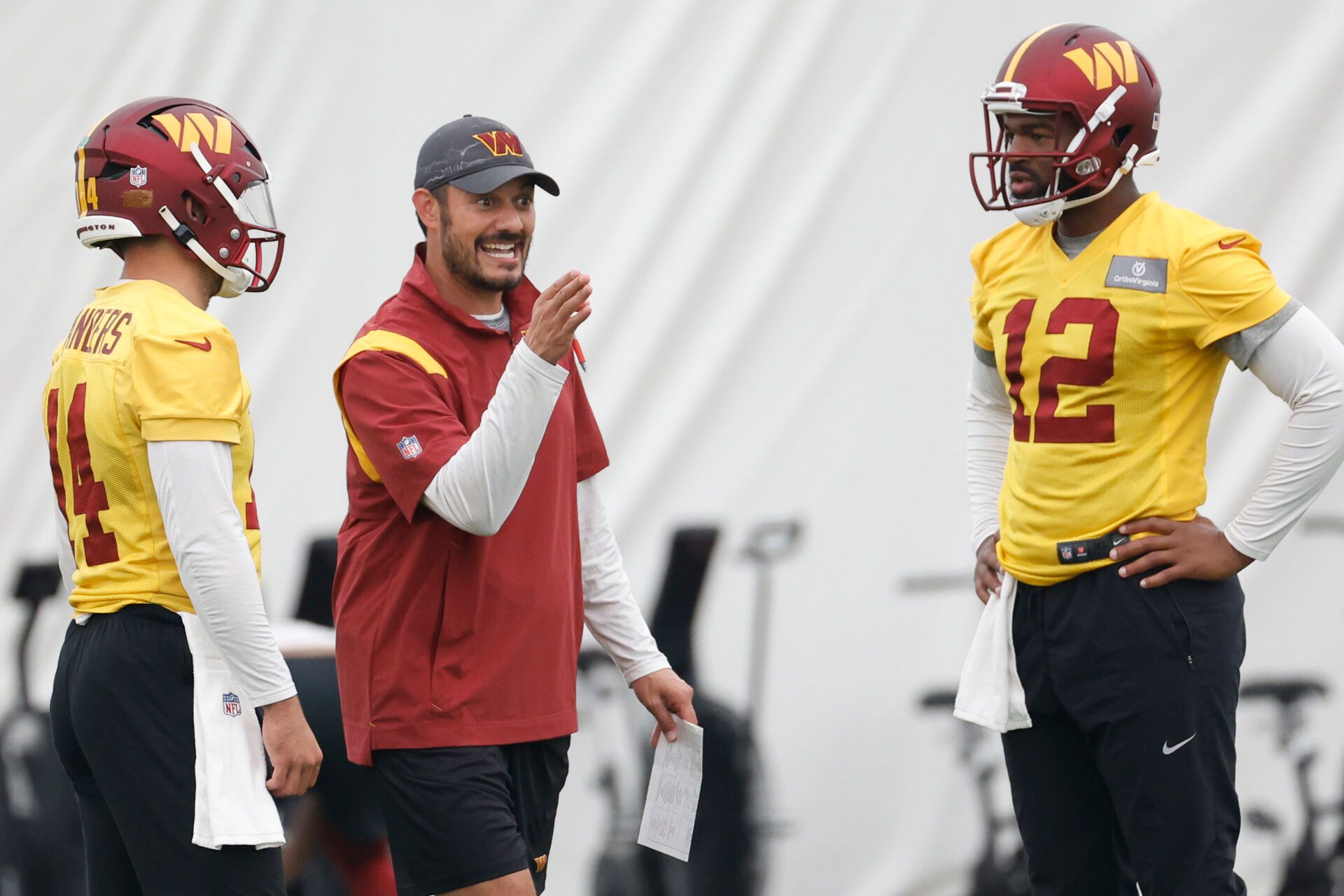 Washington Commanders quarterbacks coach Tavita Pritchard (M) talks to Commanders quarterback Sam Howell (14) and Commanders quarterback Jacoby Brissett (12) during day three of minicamp at OrthoVirginia Training Center at Commanders Park, held inside the training bubble due to poor air quality from Canadian wildfire smoke in Ashburn.