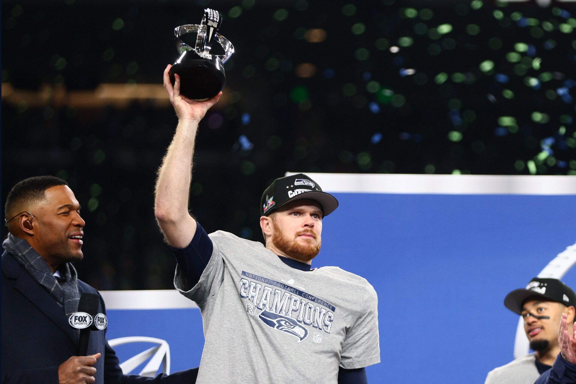 Seattle Seahawks quarterback Sam Darnold (14) celebrates with the trophy on the podium after defeating the Los Angeles Rams in the 2026 NFC Championship Game at Lumen Field.