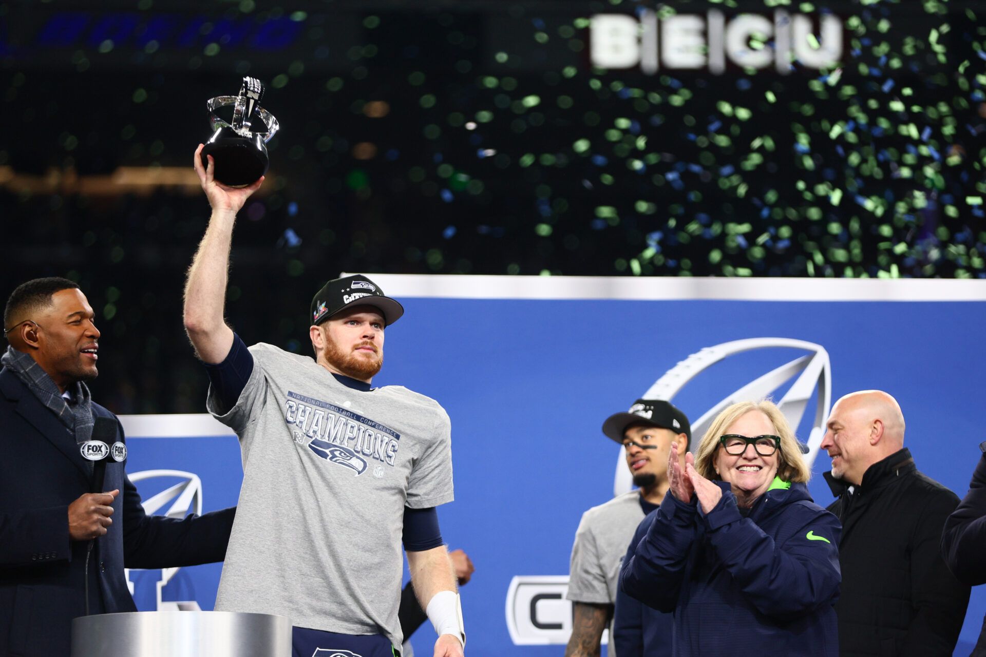 Seattle Seahawks quarterback Sam Darnold (14) celebrates with the trophy on the podium after defeating the Los Angeles Rams in the 2026 NFC Championship Game at Lumen Field.