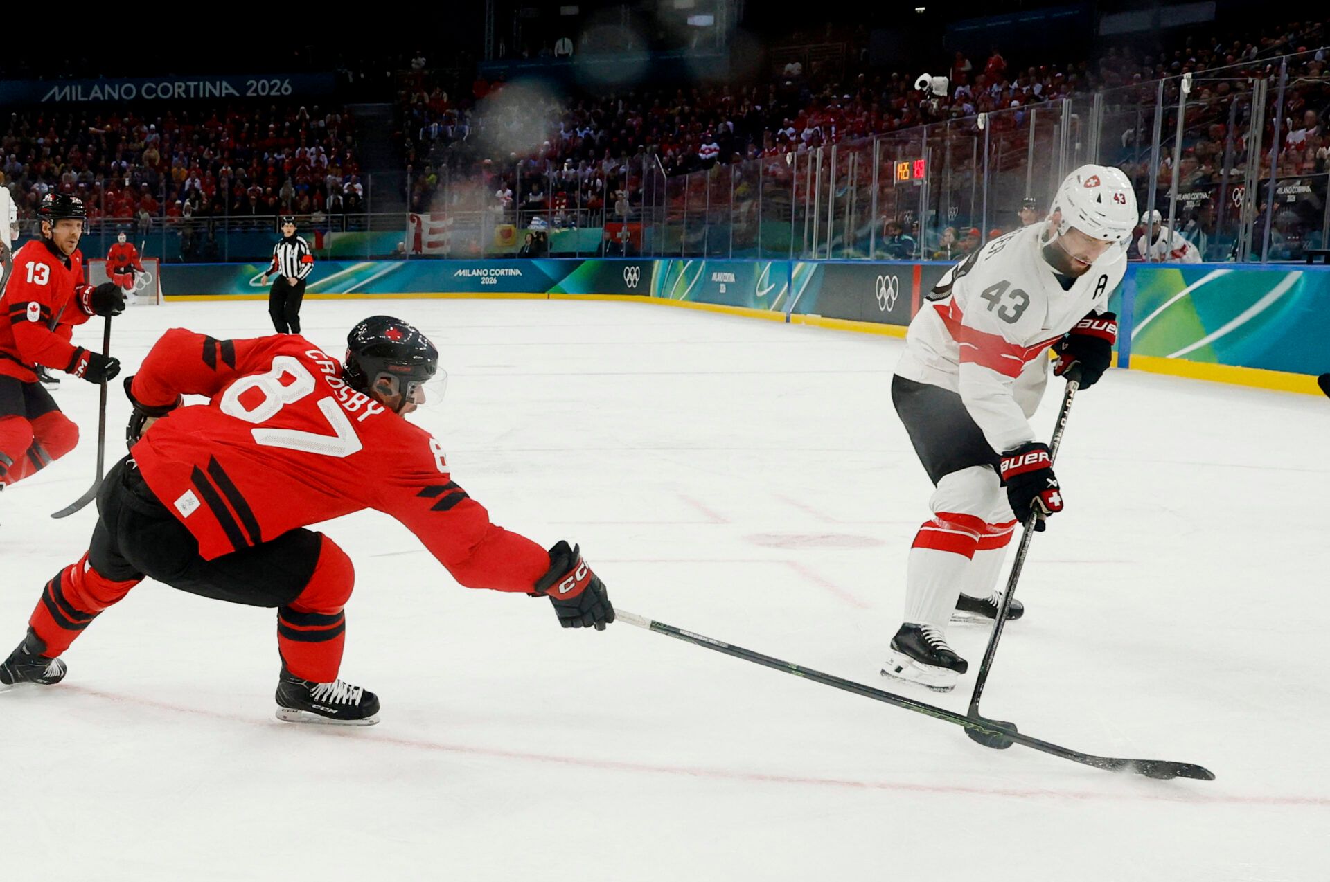 Andrea Glauser of Switzerland in action with Sidney Crosby of Canada  in men's ice hockey group A play during the Milano Cortina 2026 Olympic Winter Games at Milano Santagiulia Ice Hockey Arena.