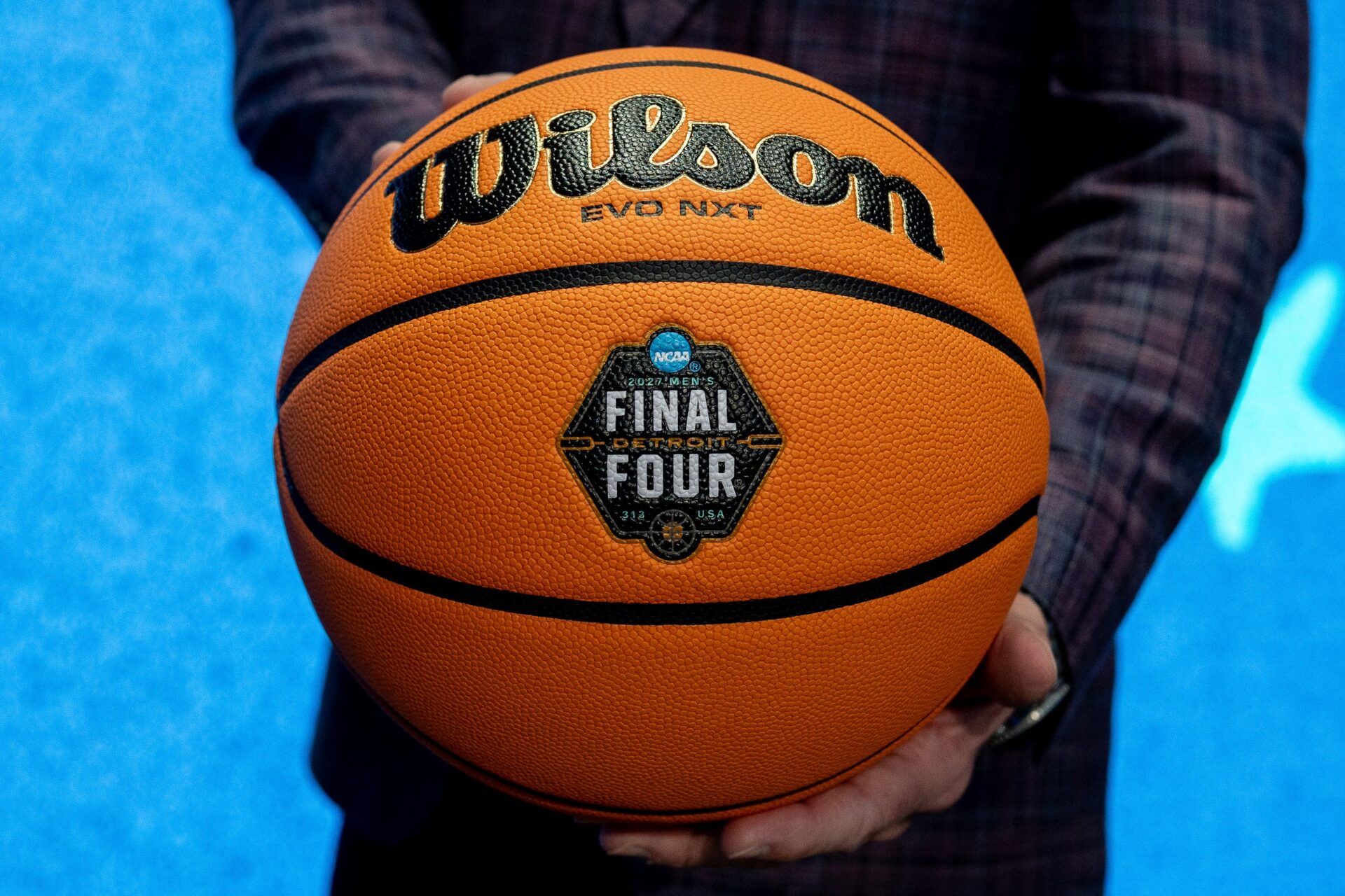 Dave Beachnau, CEO of the Detroit Local Organizing Committee, stands on stage holding a basketball featuring the newly unveiled logo for the 2027 NCAA Men’s Final Four during a press conference inside Ford Field in Detroit on Friday, Dec. 19, 2025. © David Rodriguez Muñoz / USA TODAY NETWORK via Imagn Images