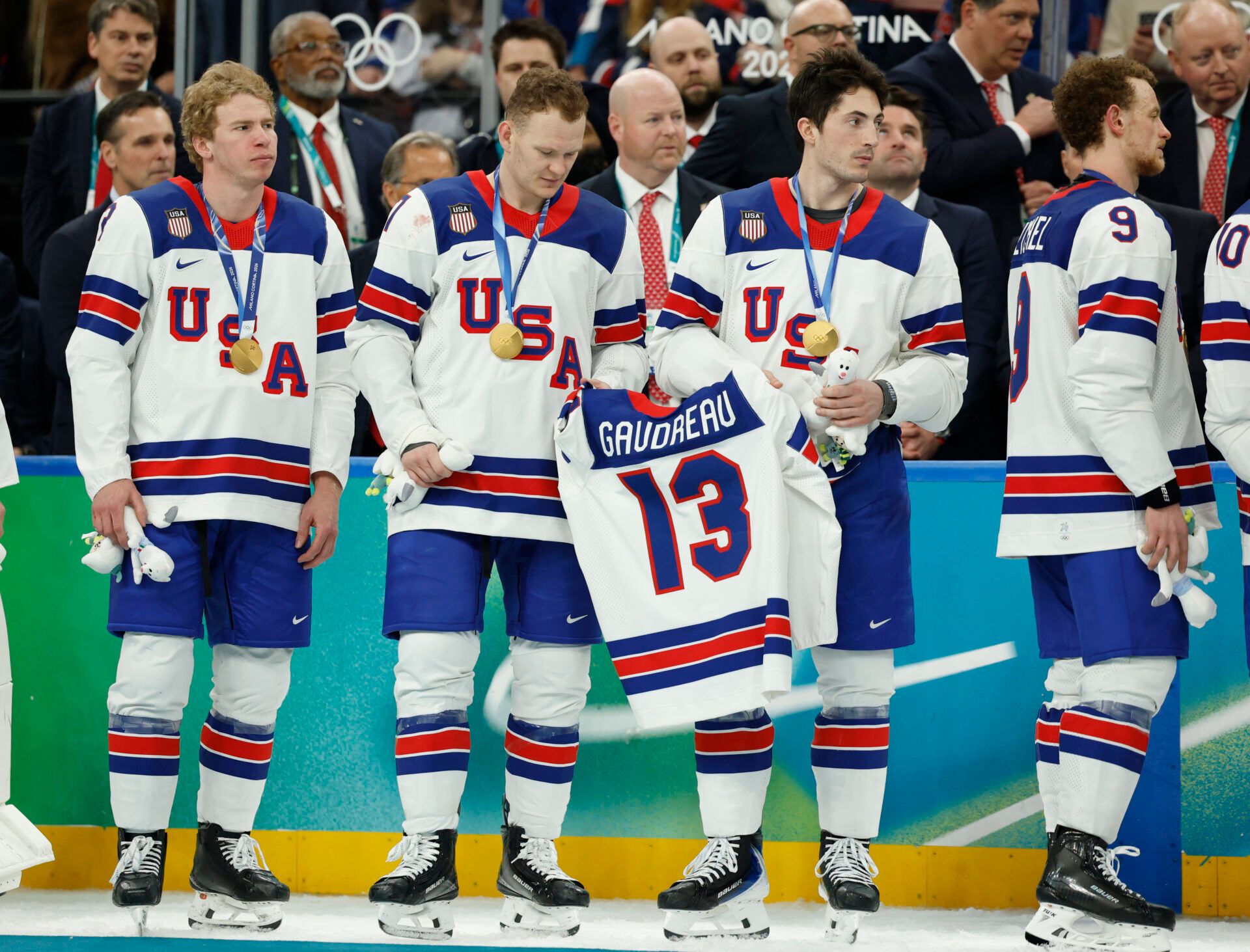 Brady Tkachuk (7) of the United States and Zach Werenski (8) of the United States hold the jersey of Johnny Gaudreau after defeating Canada in the men's ice hockey gold medal game during the Milano Cortina 2026 Olympic Winter Games at Milano Santagiulia Ice Hockey Arena.