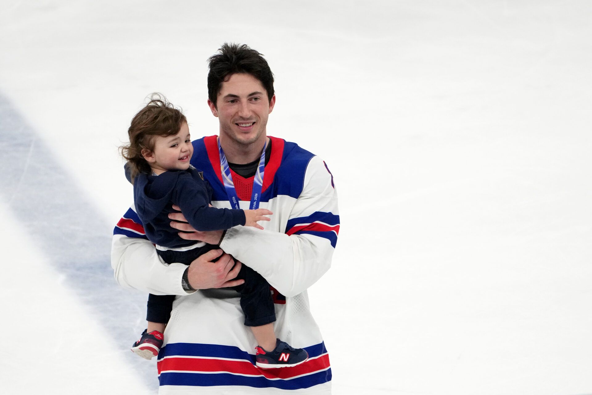 Zach Werenski of the United States celebrates while holding Johnny Gaudreau Jr, the son of the late Johnny Gaudreau after winning the men's ice hockey gold medal game during the Milano Cortina 2026 Olympic Winter Games at Milano Santagiulia Ice Hockey Arena.