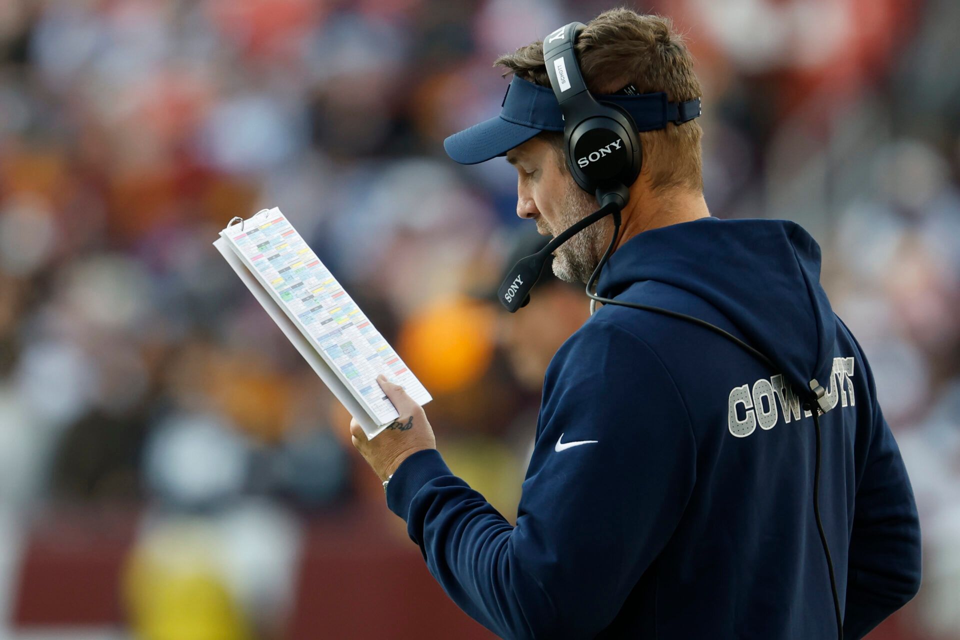 Dallas Cowboys head coach Brian Schottenheimer looks at his play sheet on the sidelines against the Washington Commanders during the second half at Northwest Stadium.