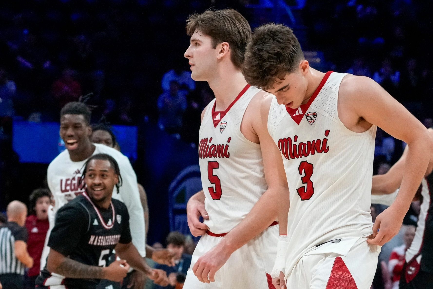 Miami RedHawks guard Peter Suder (5) and guard Luke Skaljac (3) leave the floor as UMass Minutemen forward Leonardo Bettiol (3) celebrates a win after the final buzzer of the second half of Mid-American Conference Tournament first round game between the Miami RedHawks and the UMass Minutemen at Rocket Arena in Cleveland on Thursday, March 12, 2026. Top-seeded Miami was eliminated from the tournament with an 87-82 loss to the Minutemen.
