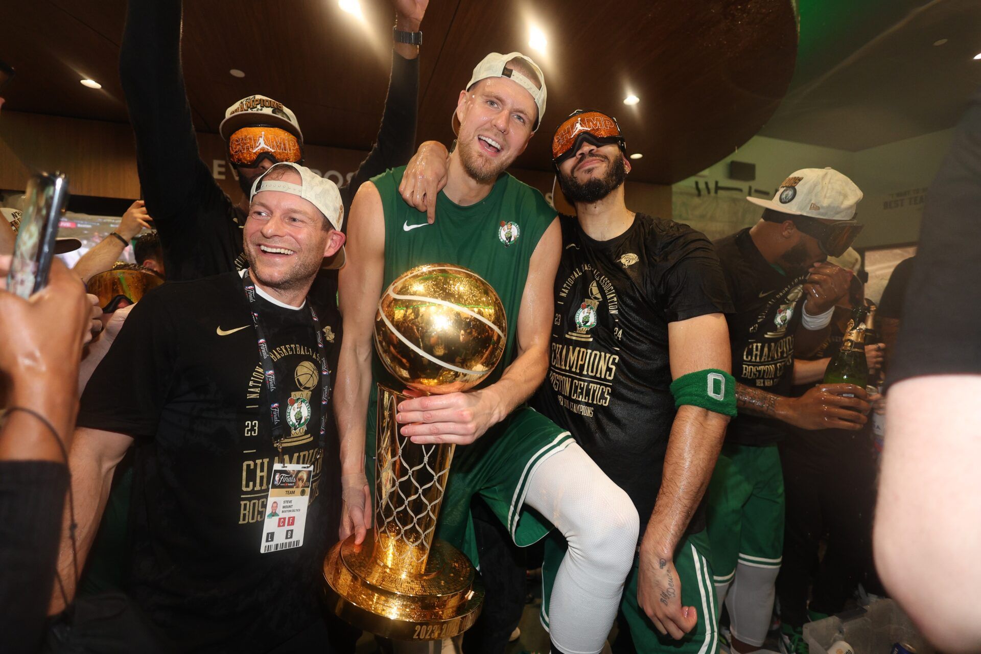 Boston Celtics center Kristaps Porzingis (center) and forward Jayson Tatum (right) celebrate with Celtics director of rehabilitation Steve Mount in the locker room after winning the 2024 NBA Finals against the Dallas Mavericks at TD Garden.