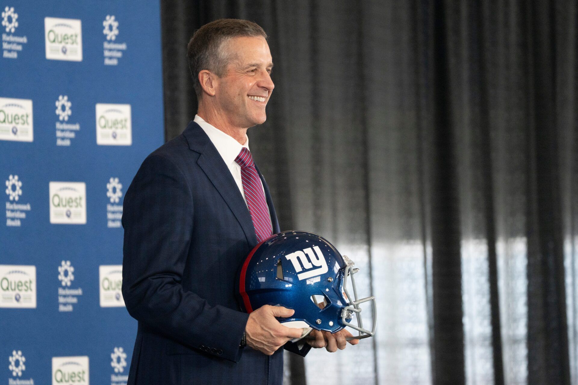 New Giants Head Coach John Harbaugh holds up a New York Giants helmet during a press conference welcoming Harbaugh at the Quest Diagnostics Training Center in East Rutherford on Tuesday, Jan. 20, 2025.