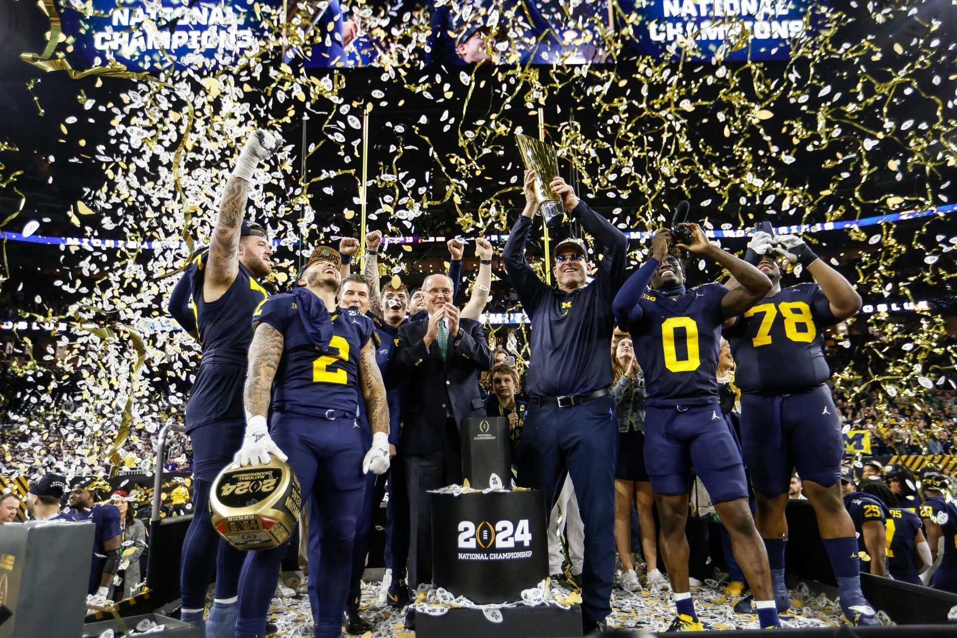 Michigan head coach Jim Harbaugh lifts up the trophy as players and coaches celebrate after 34-13 win over Washington to win the national championship game at NRG Stadium in Houston on Monday, Jan. 8, 2024.